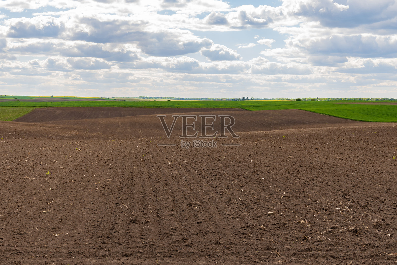 广阔的耕地在充满云彩的蔚蓝天空下延展,显示出农村地区为下一个种植季节的准备。照片摄影图片