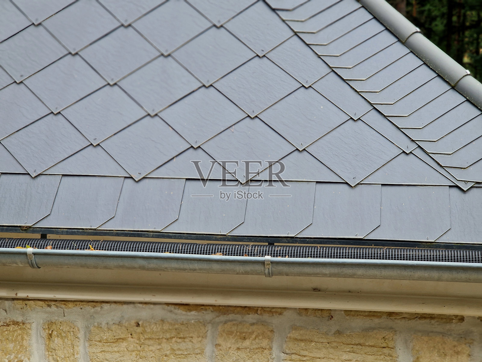 设计良好的塑料网覆盖在排水沟内部,树叶不会掉入其中。堵塞的排水管已成为过去。烧制的屋顶瓦。照片摄影图片