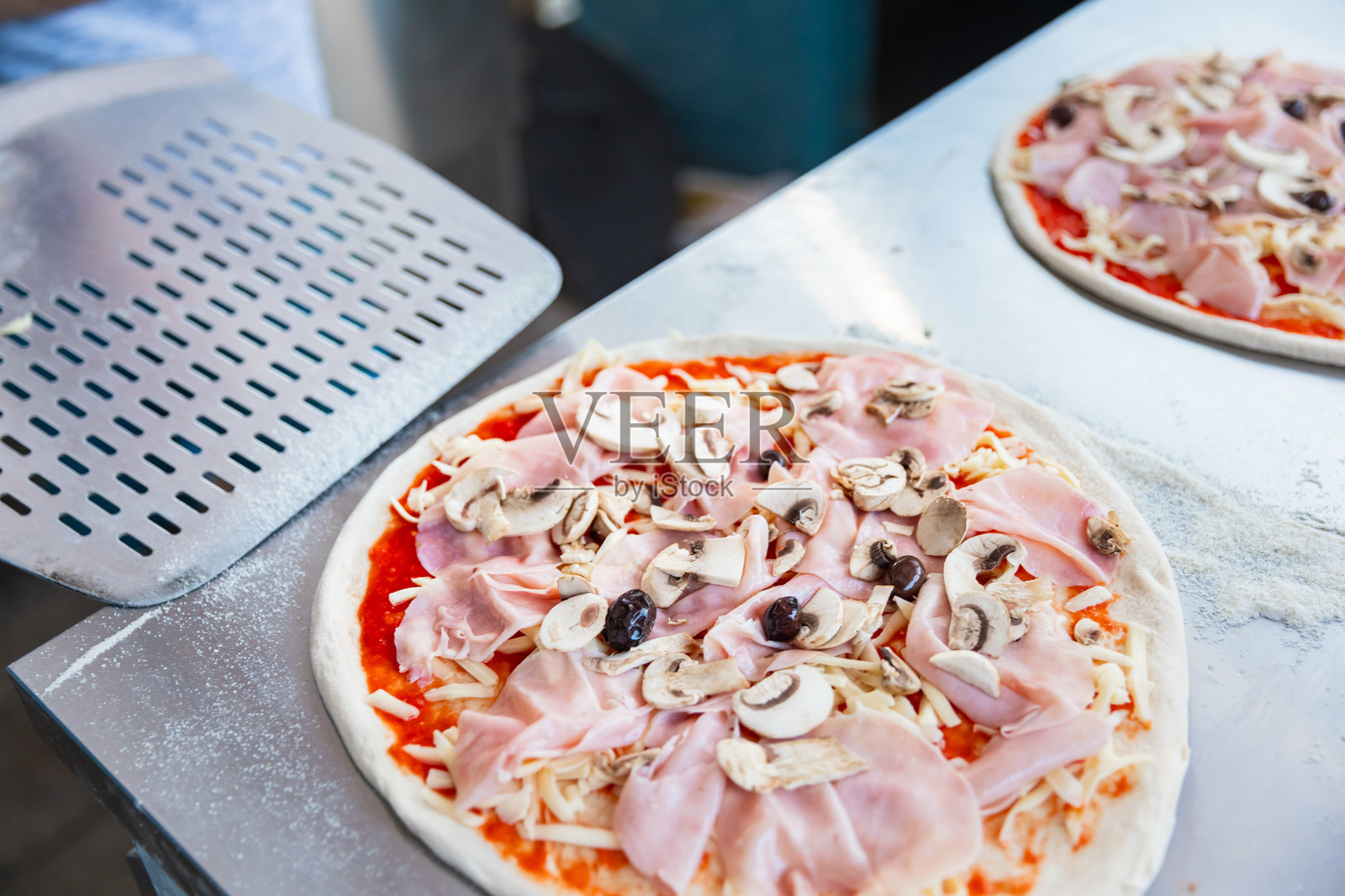 户外厨房阳光明媚的日子,披萨厨师(披萨师傅)将披萨放在铲子上准备放入砖炉中。照片摄影图片