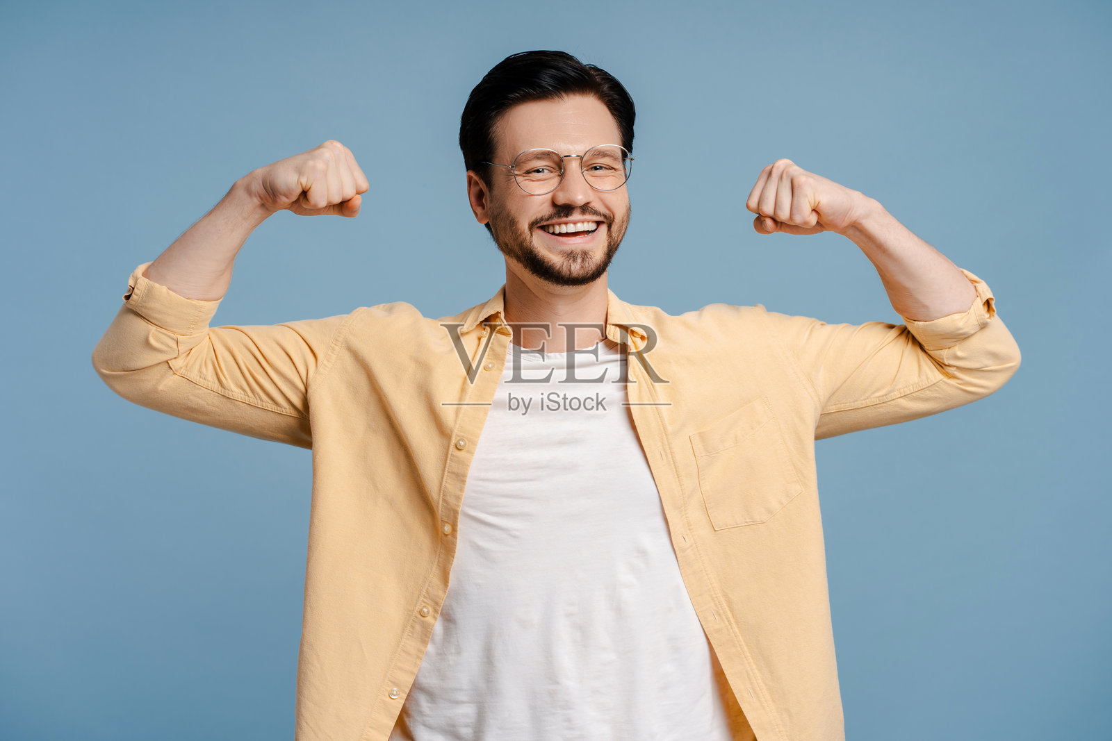 快乐微笑的络腮胡男子在蓝色背景下展示肌肉照片摄影图片