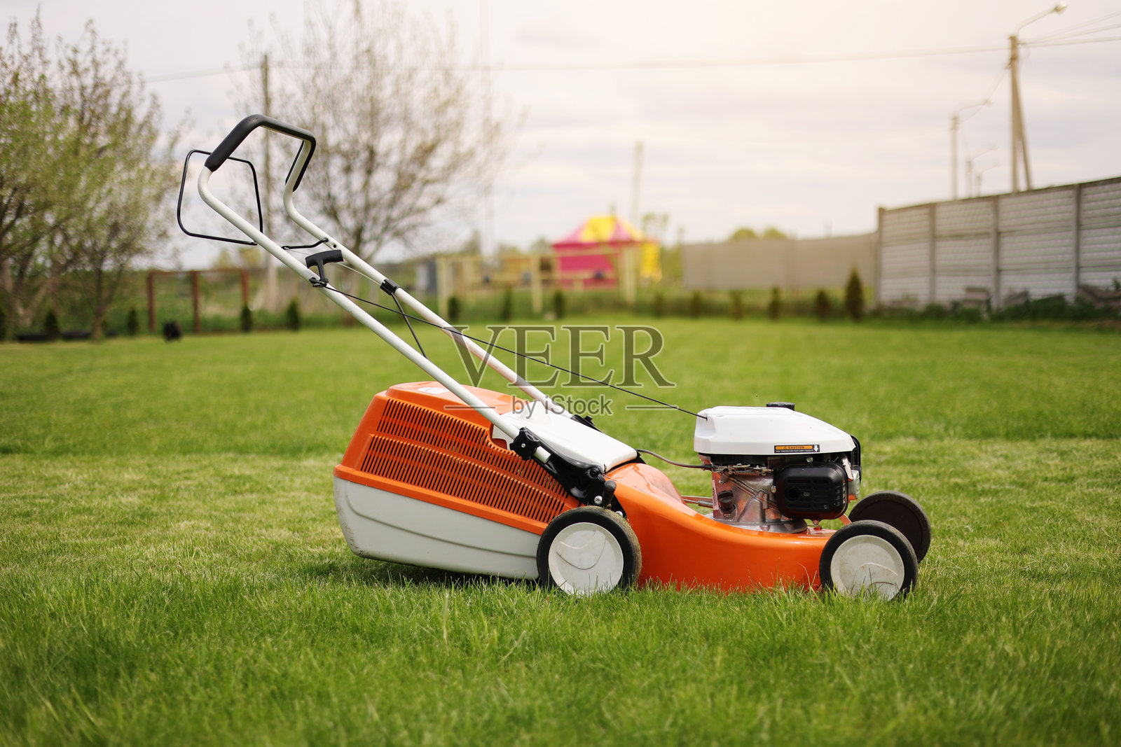 现代橙灰色电动割草机侧视图正在修剪明亮丰盛的绿色草坪。园艺工具。旋转割草机在草坪上。专业草坪护理服务。文本位置。照片摄影图片