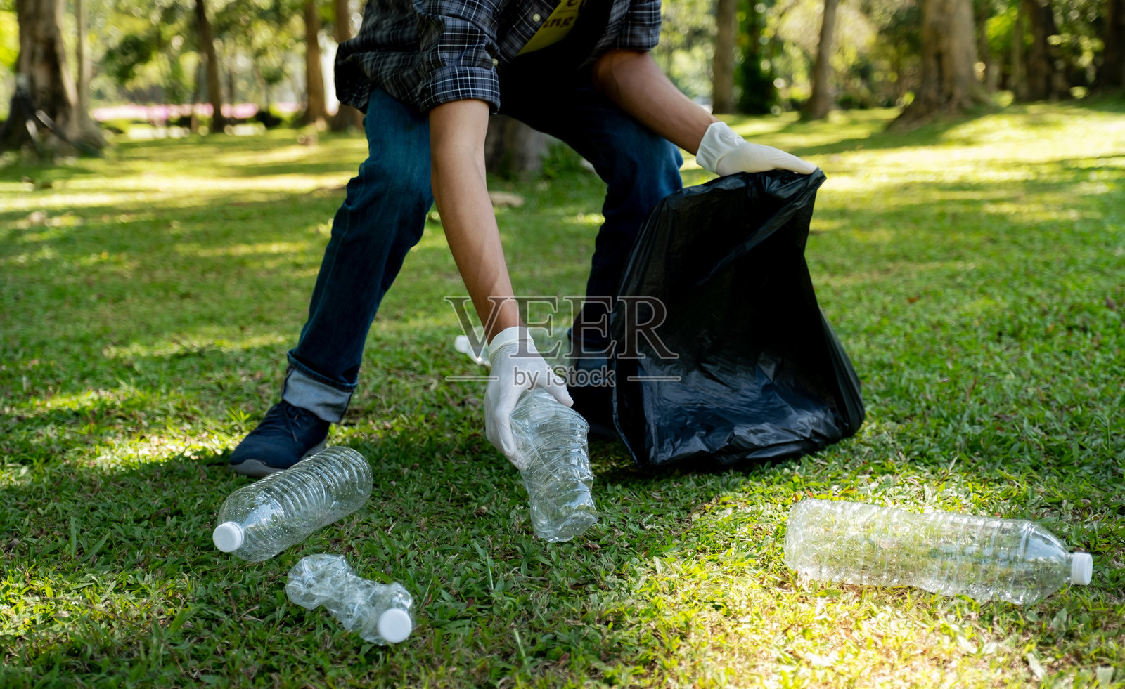 手拿塑料瓶废品,在公园捡拾垃圾并放入黑色垃圾袋,环境保护地球日照片摄影图片