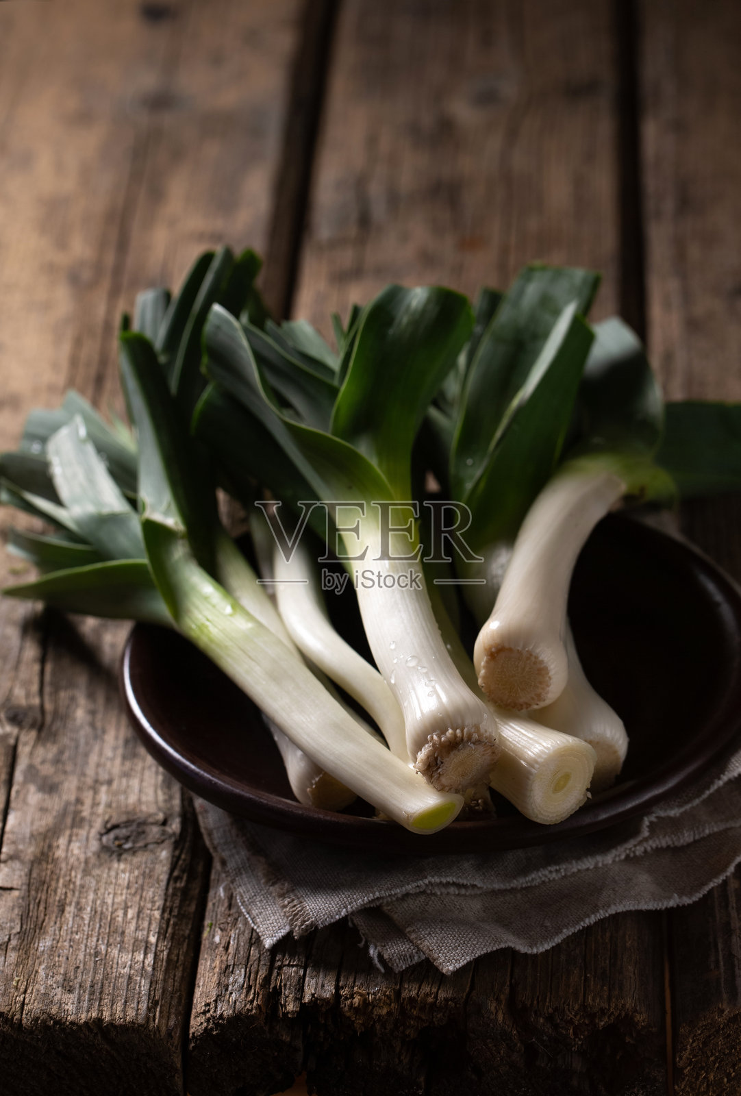 一束绿色韭菜放在桌角的棕色碗里照片摄影图片