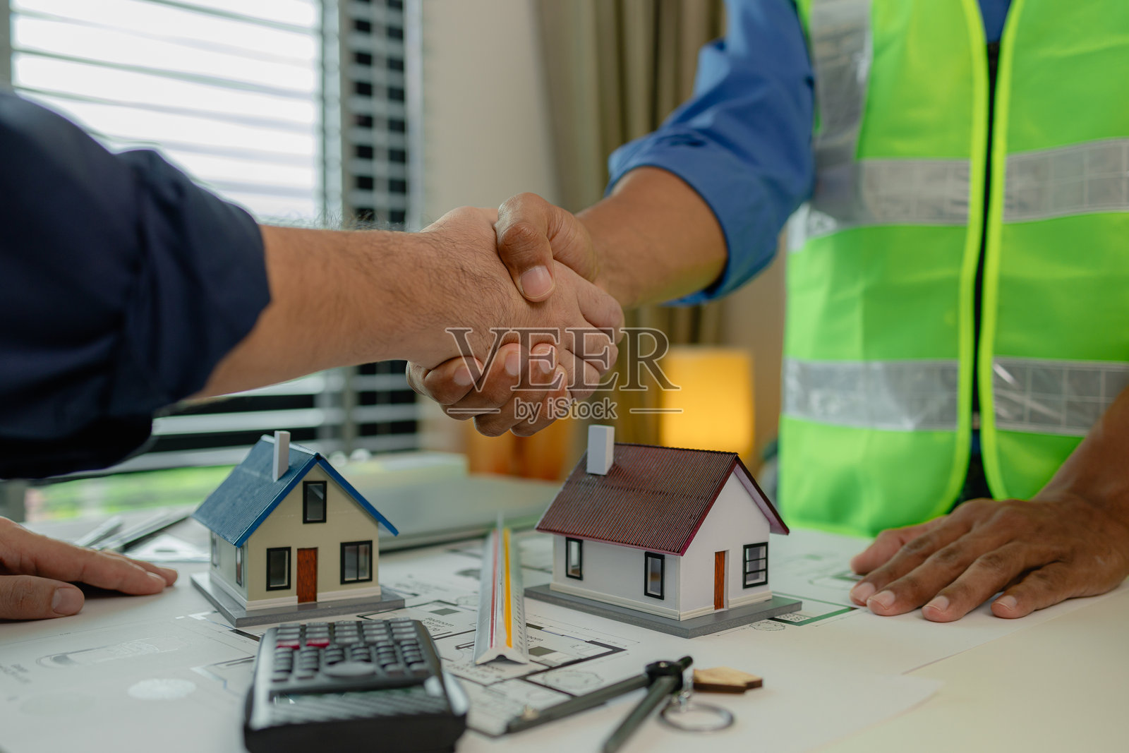 工程师和建筑师握手庆祝,因为他们刚刚完成了一个大型建筑项目,两位工程师在会议后握手,桌子上放着蓝图。照片摄影图片