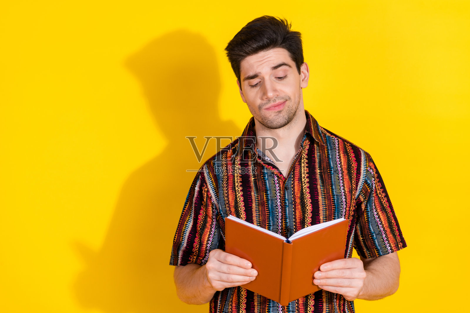 年轻男子穿着衬衫,独自一人在黄色背景下阅读书籍,沉思。照片摄影图片