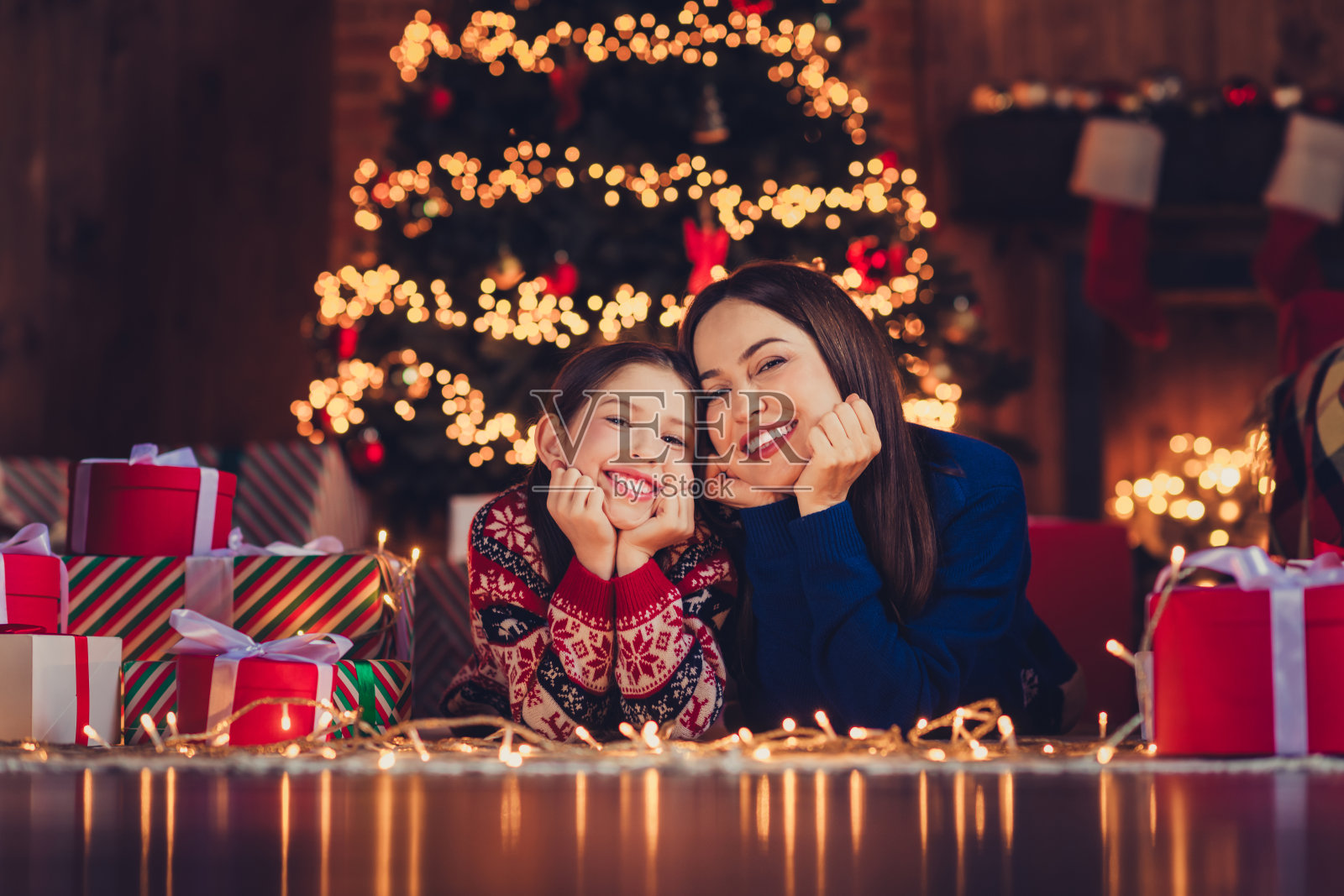 全身照,漂亮的小女儿和妈妈梦幻般地躺在地板上,穿着圣诞服装,享受室内公寓的圣诞派对装饰。照片摄影图片