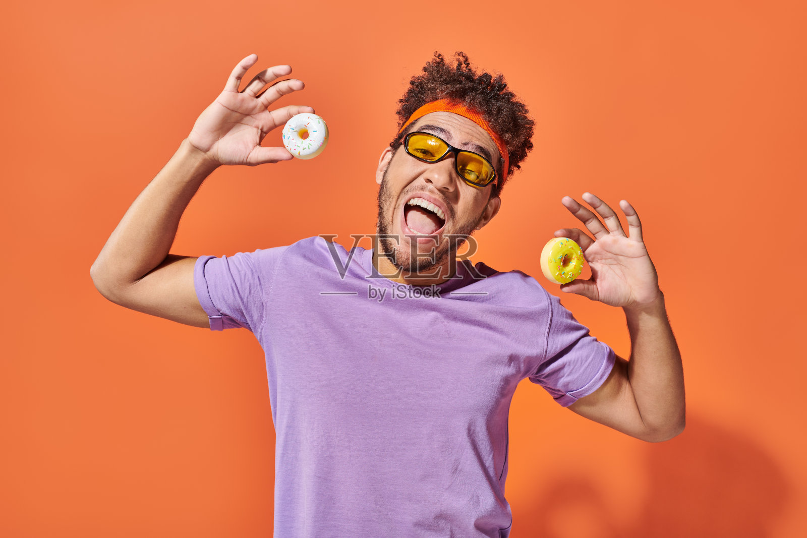 一位年轻帅气的男士兴奋地手持甜甜圈,展现出欢乐的氛围照片摄影图片