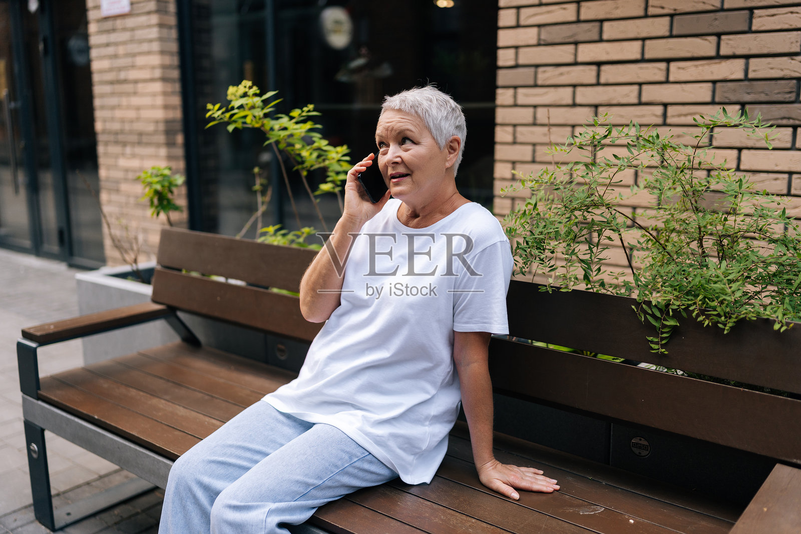 老年女性在城市户外长椅上放松,使用智能手机。欧洲的灰发老年女性在退休期间享受闲暇时光。照片摄影图片