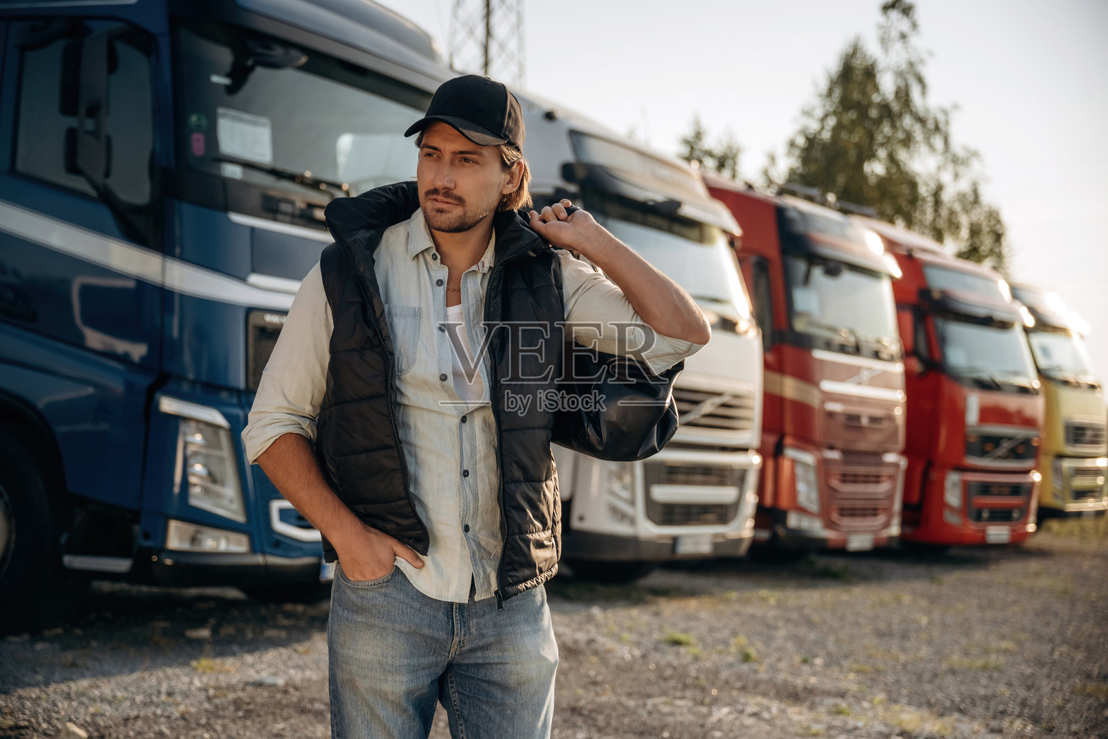 戴帽子的模特在摆姿势。卡车司机在户外靠近运输车辆。照片摄影图片