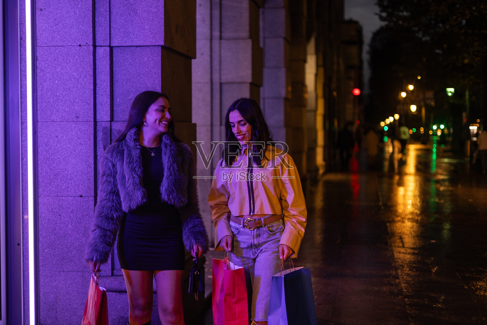 两个年轻的拉丁裔女性在雨夜里提着购物袋逛时装店照片摄影图片