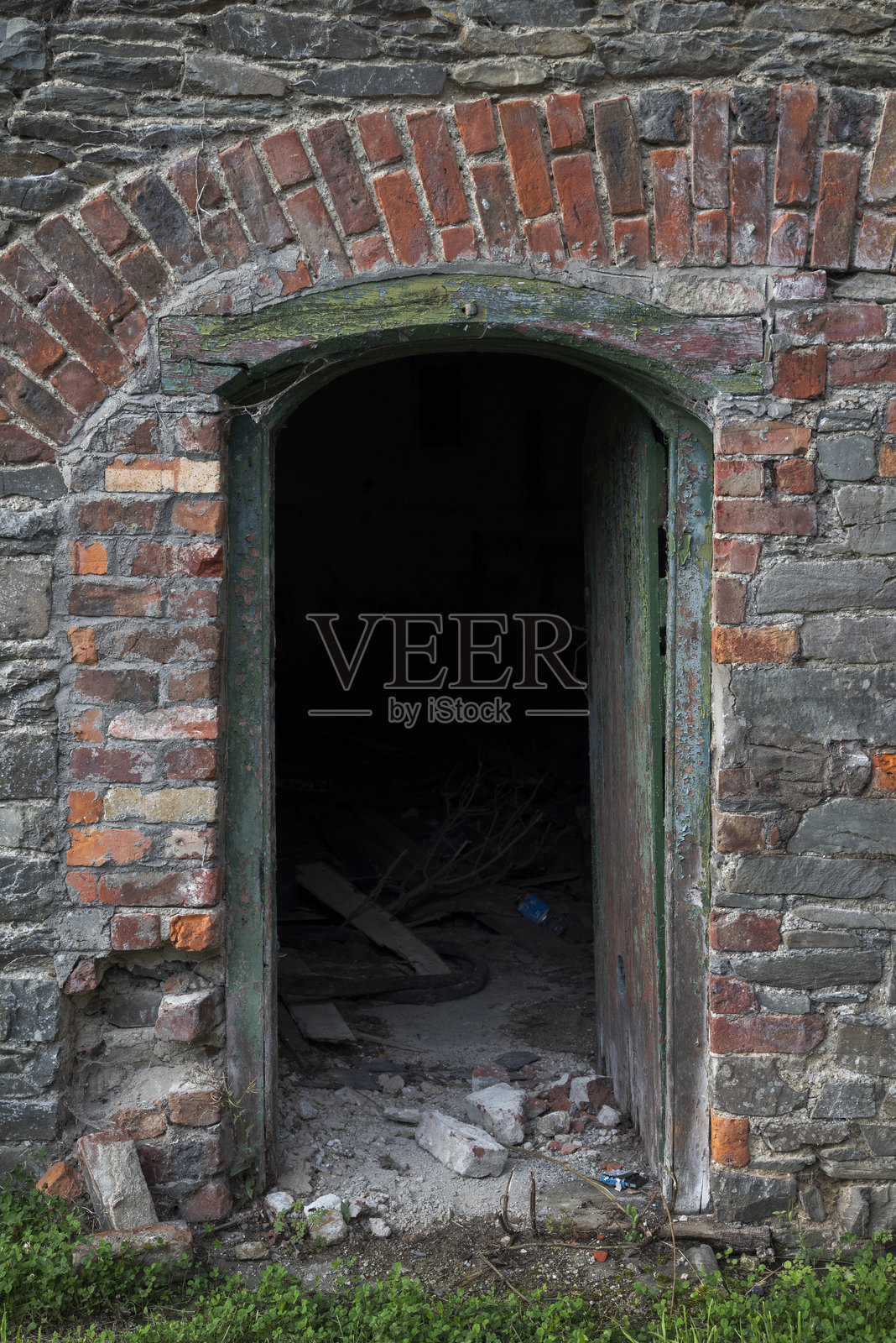 一扇绿色木门微微开启,镶嵌在石墙中。照片摄影图片