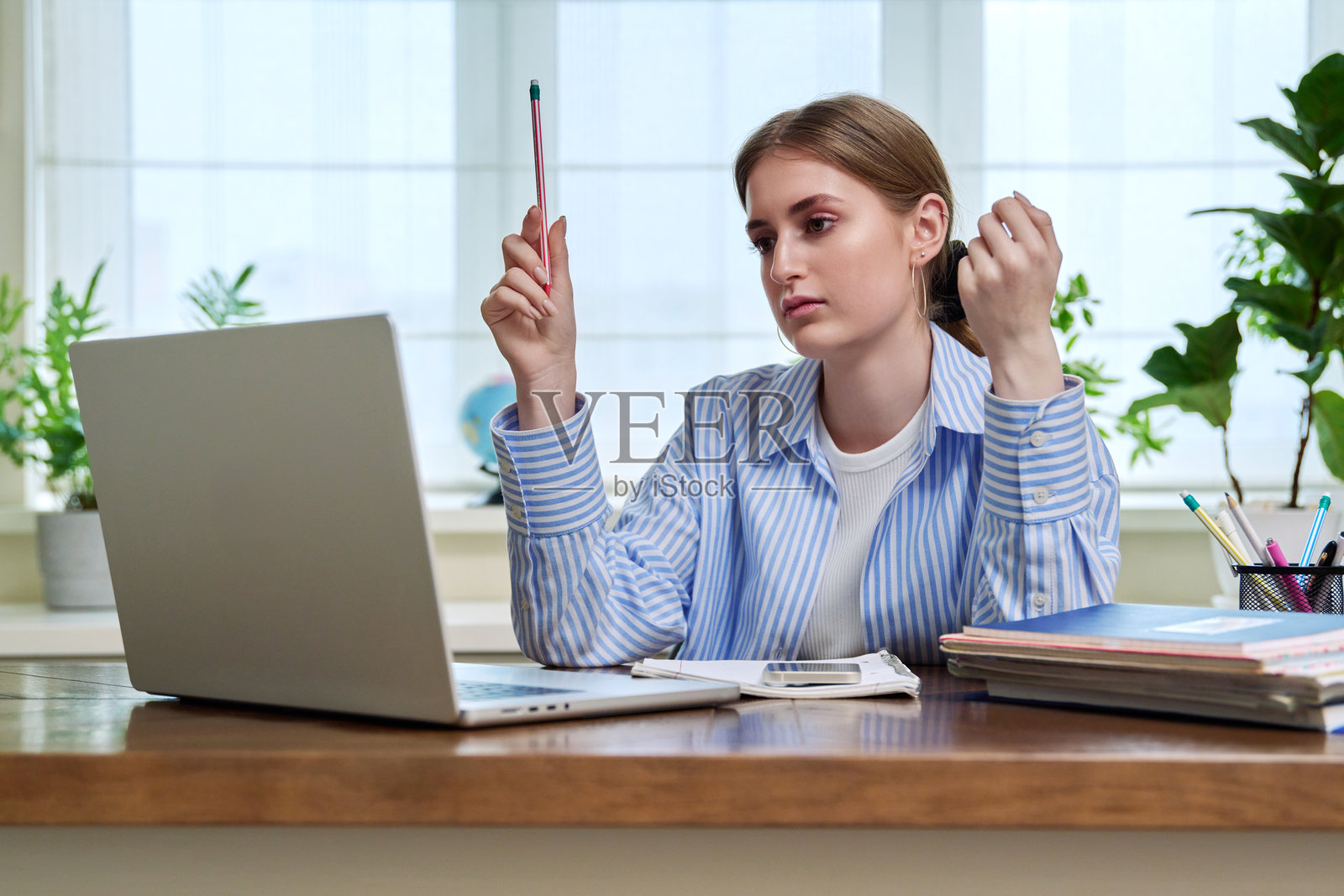 在家中书桌前坐着的少女学生,使用笔记本电脑进行视频会议学习。照片摄影图片