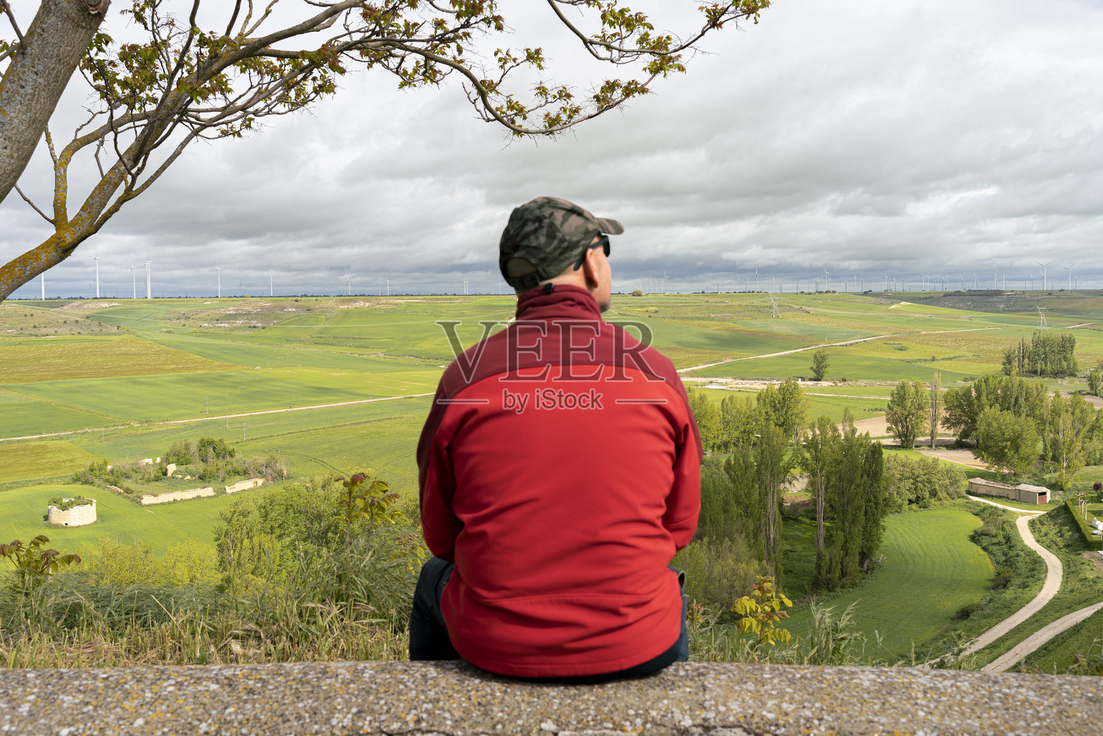 一位坐着的男子观察着一片广阔的绿色景观,天空中乌云密布,似乎要下雨。照片摄影图片
