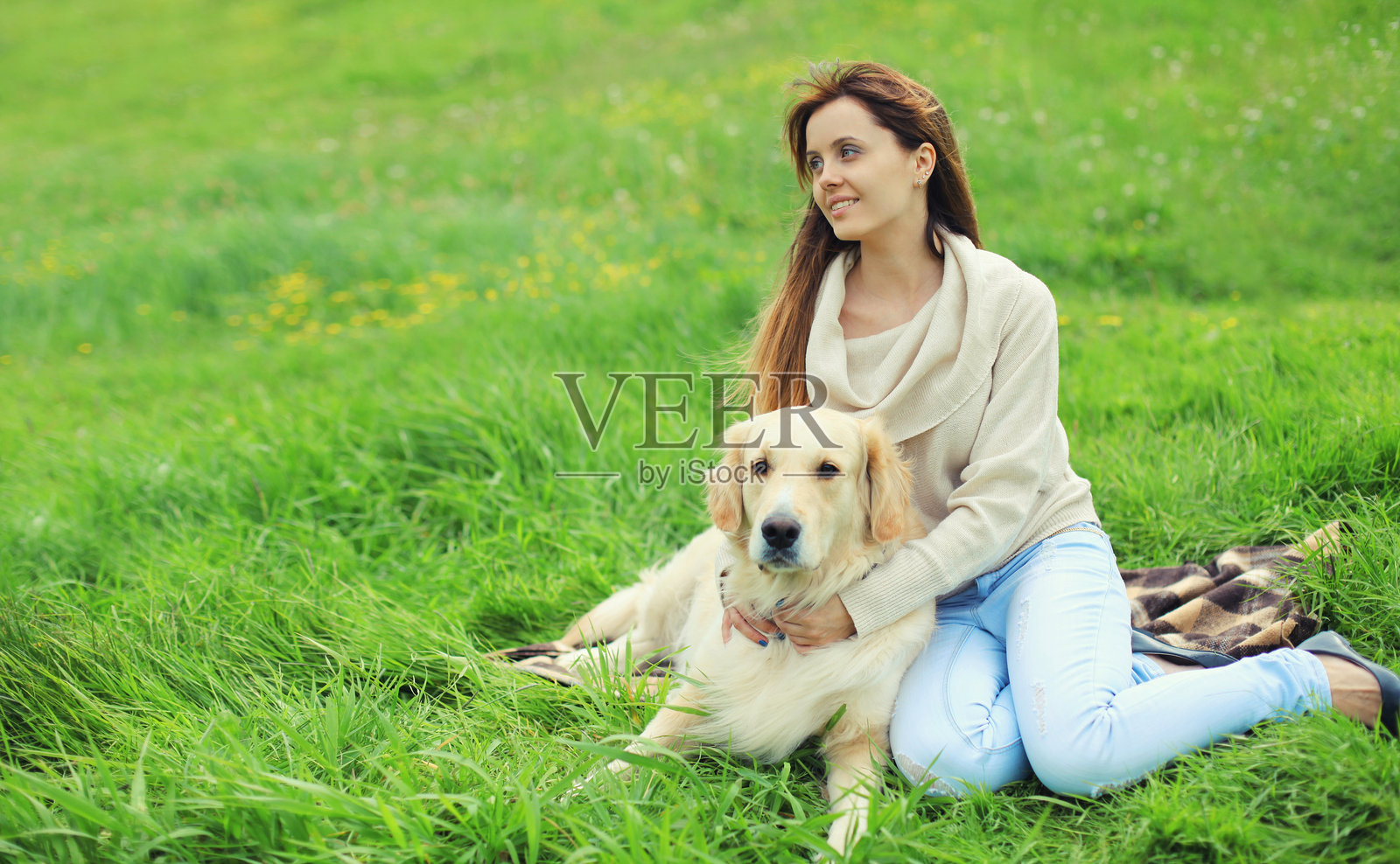 年轻女性快乐地与金毛猎犬一起坐在夏季公园的草地上照片摄影图片