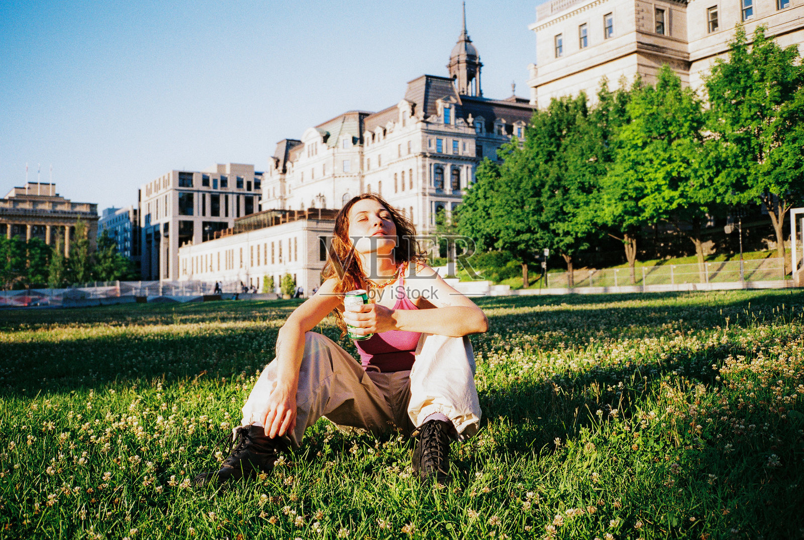 在蒙特利尔的草坪上坐着的女人,手里拿着饮料罐,享受阳光。照片摄影图片
