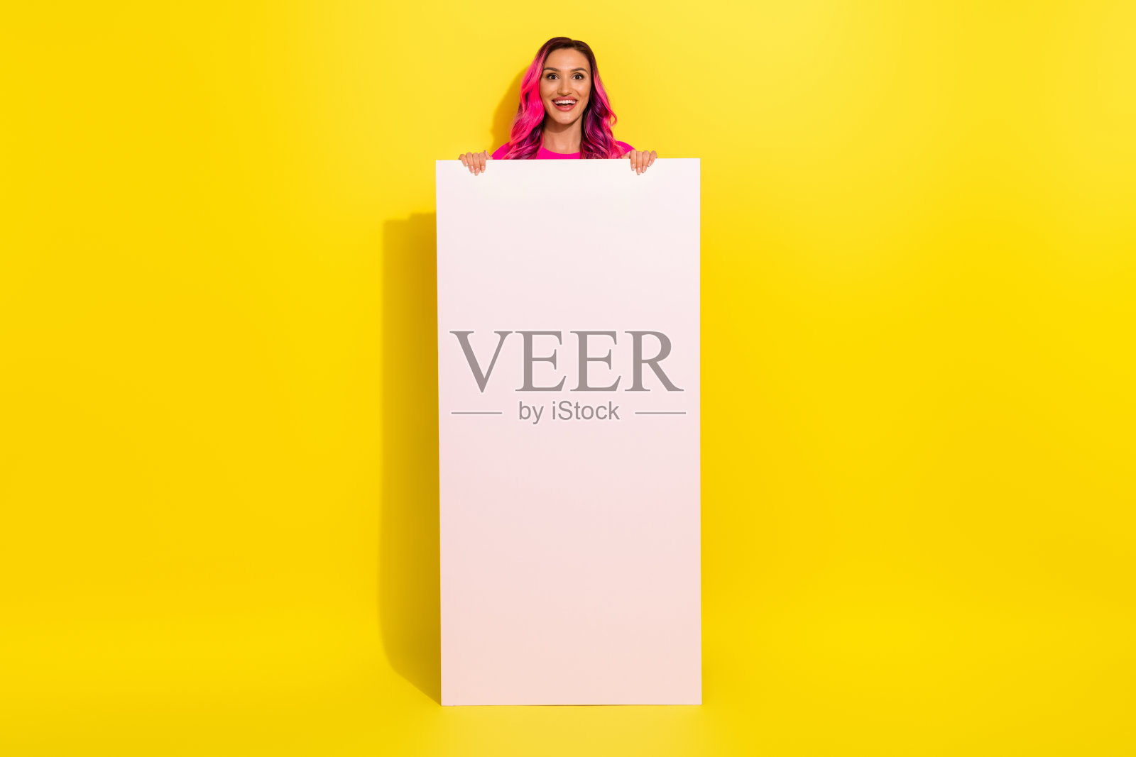 穿着毛衣的搞笑女孩全身照,面露惊讶,手持现代小工具,背景为空白的黄色。照片摄影图片