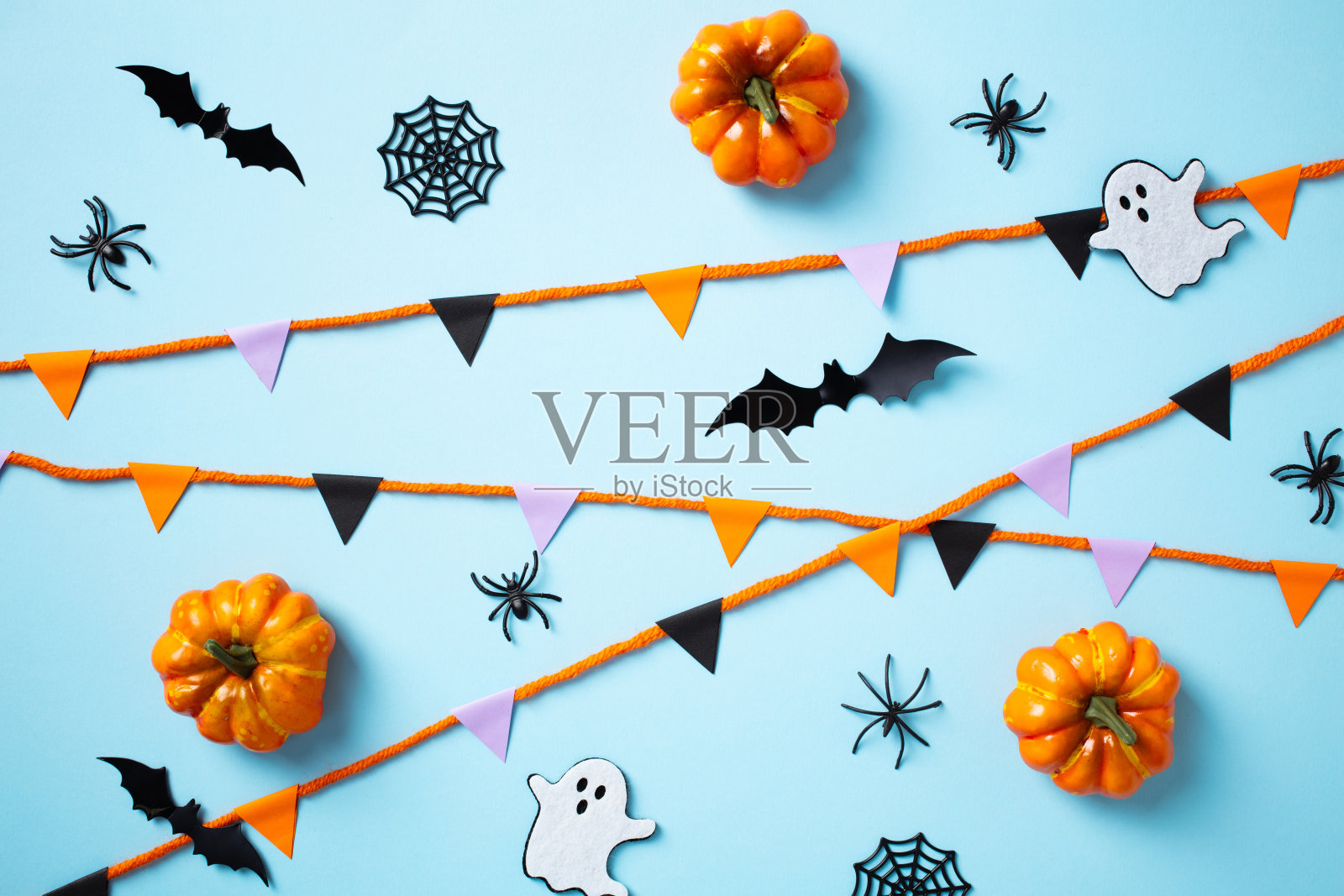 万圣节快乐的节日概念。蓝色背景上的扁平布局,包含彩旗、南瓜、鬼魂、蝙蝠和蜘蛛。照片摄影图片