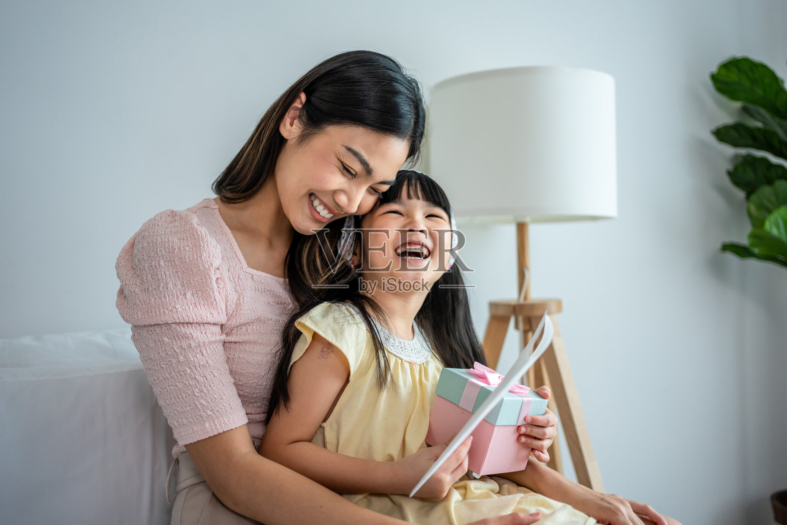 亚洲可爱的女儿给迷人的妈妈送上手工卡片。幸福的家庭,年轻的小女孩在母亲节假期里给妈妈送上惊喜明信片和礼物。照片摄影图片