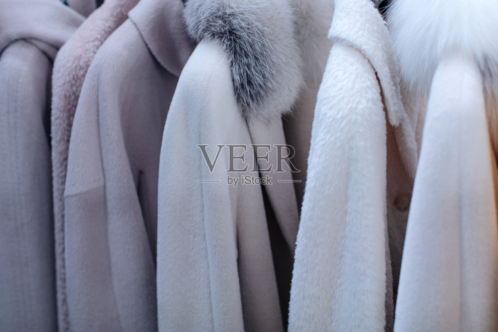 冬季奢侈服装精品店中挂着一排白色和灰色毛皮外套。照片摄影图片