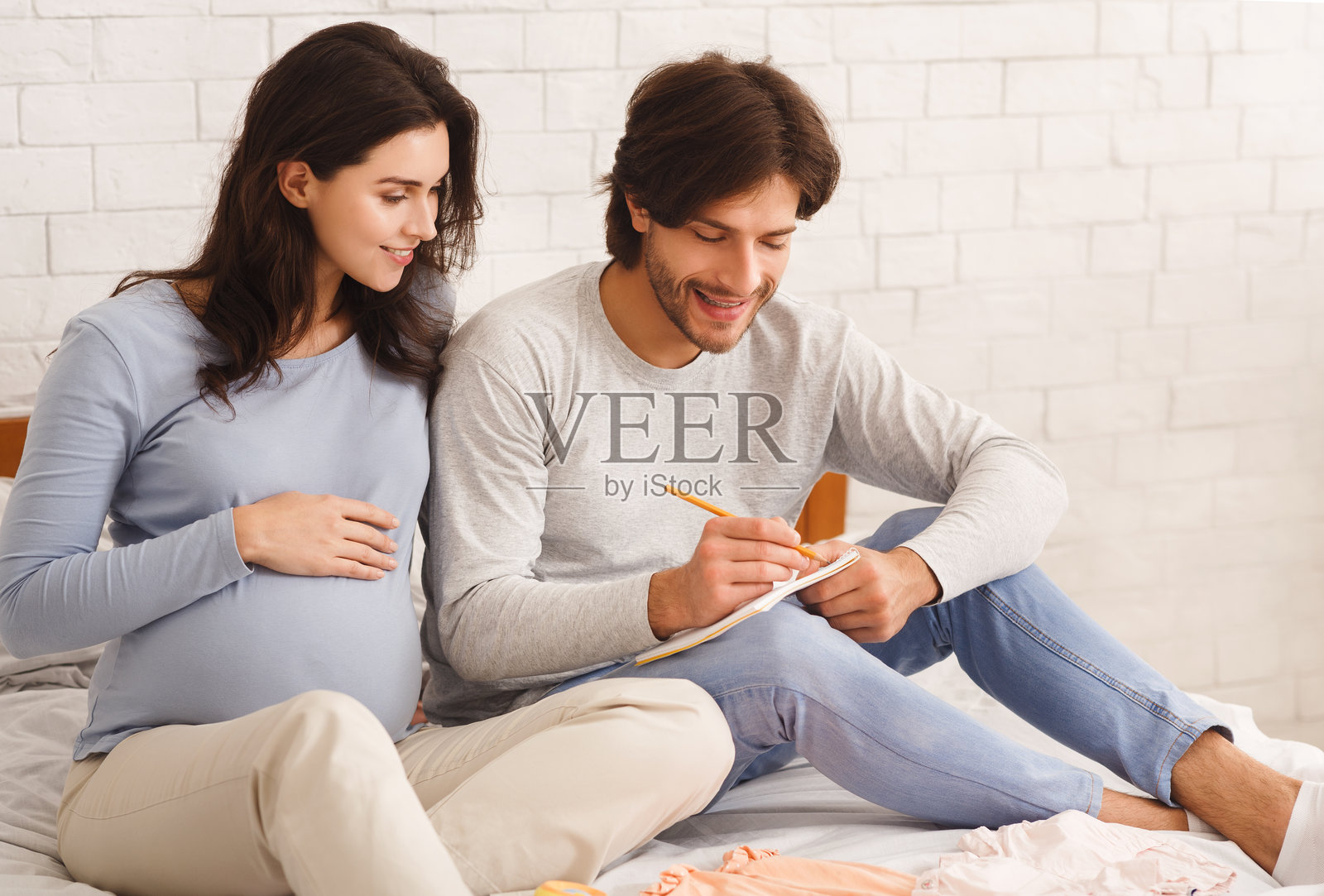 年轻的孕妇夫妇坐在床上一起选择宝宝名字照片摄影图片
