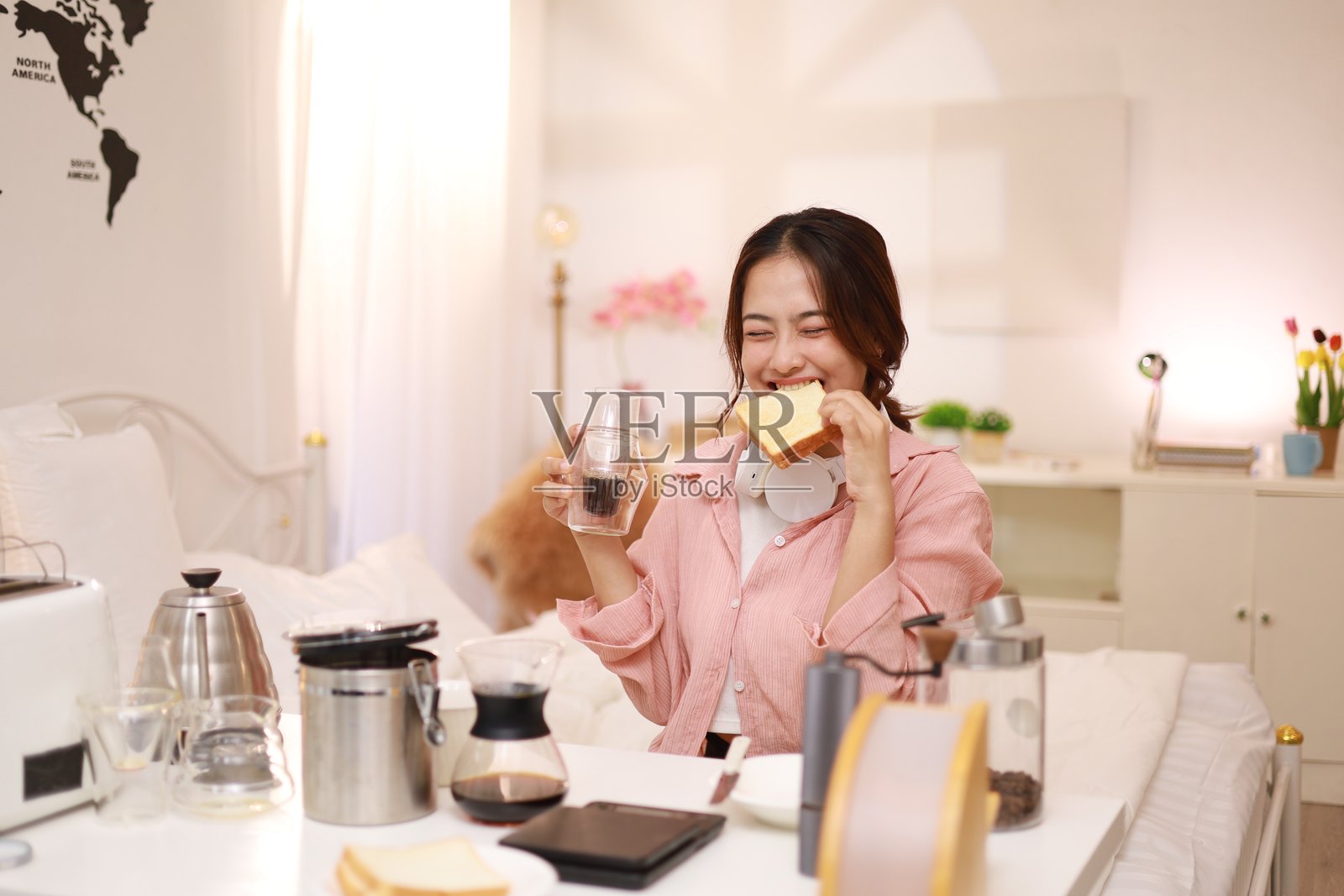 一位美丽微笑的年轻女性在早晨快乐地制作咖啡和吃面包。照片摄影图片