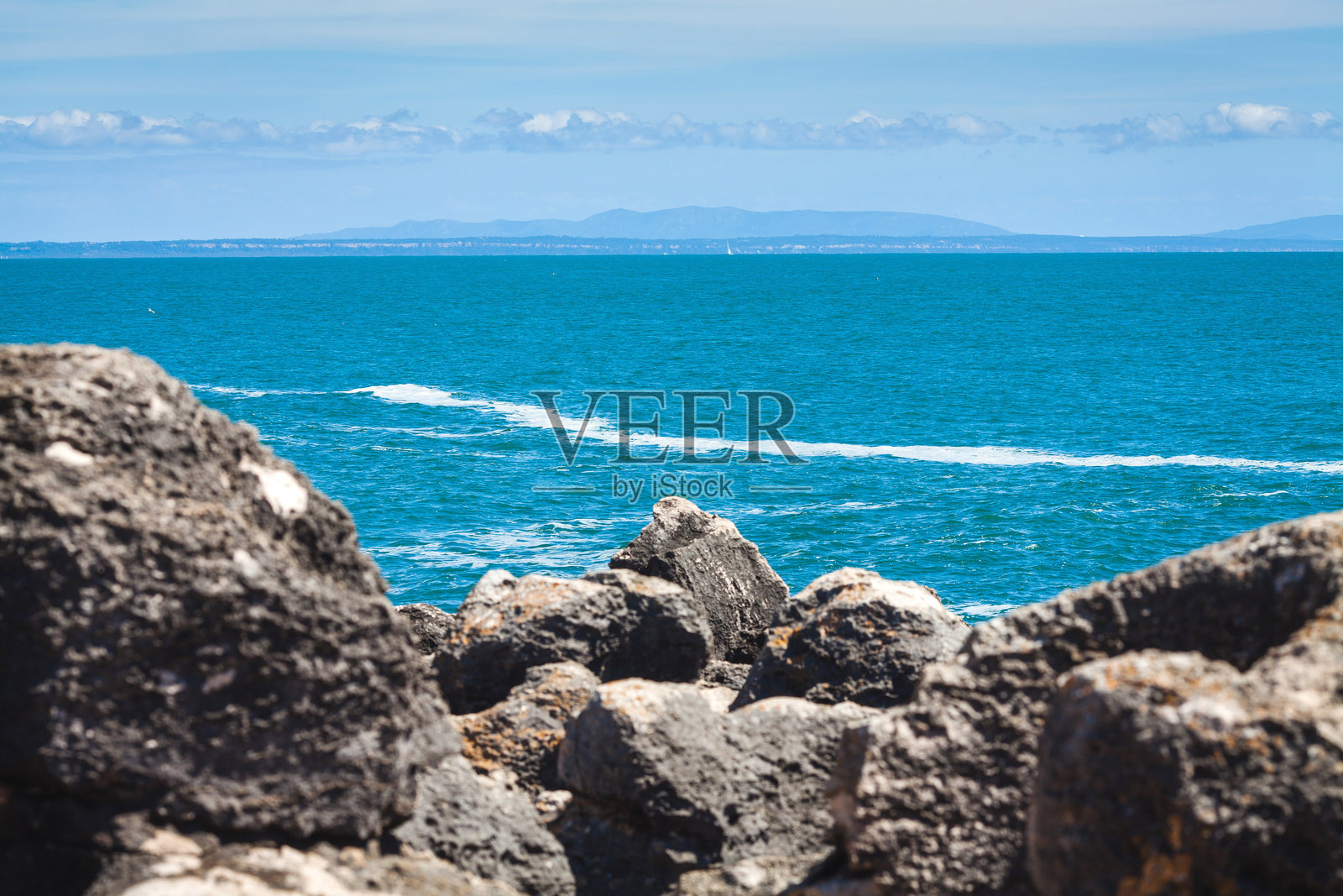 宁静的海洋场景,波光粼粼的蓝色海水延伸至地平线,前景有岩石形成,孤独的岩石从波浪中浮现,营造出宁静的氛围。照片摄影图片