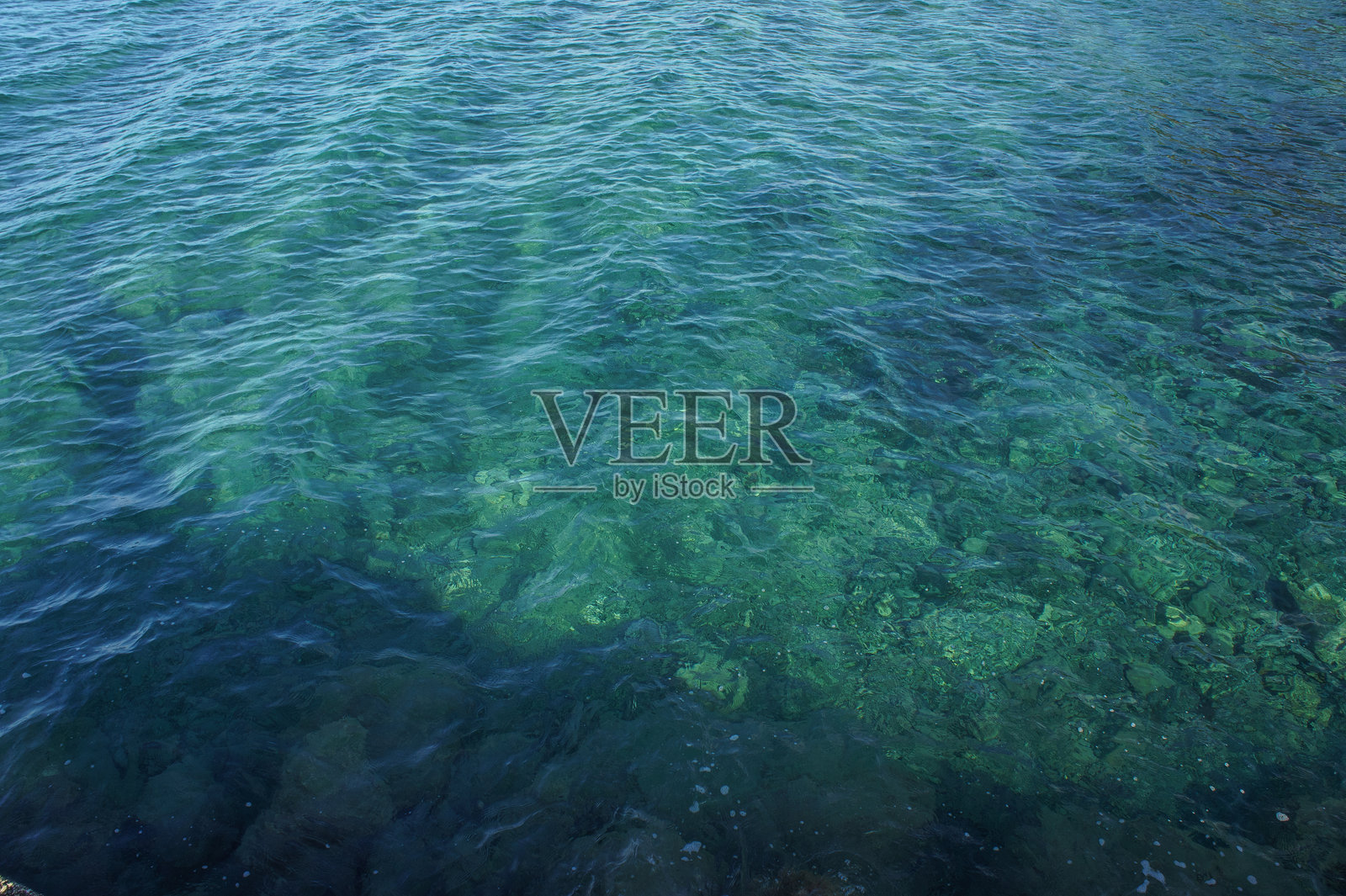 清澈的蓝色海水在平静的日子里轻轻拍打着岩石照片摄影图片