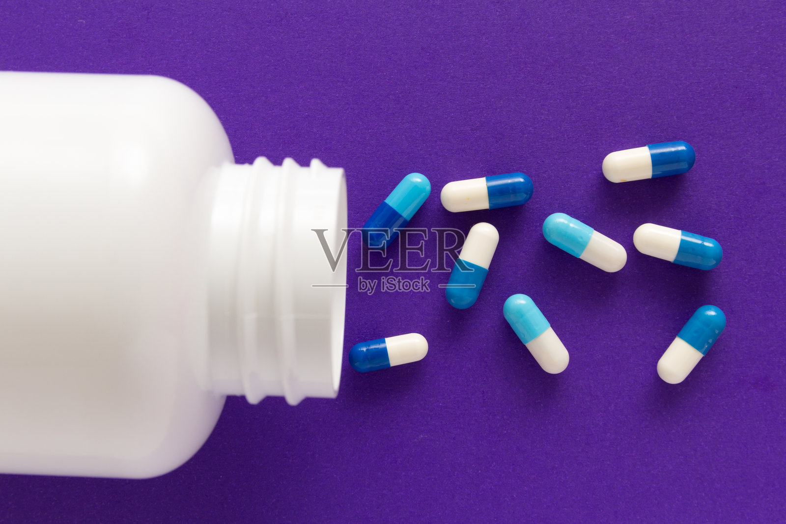 从瓶子里洒落的药物俯视图,背景为紫色桌面照片摄影图片