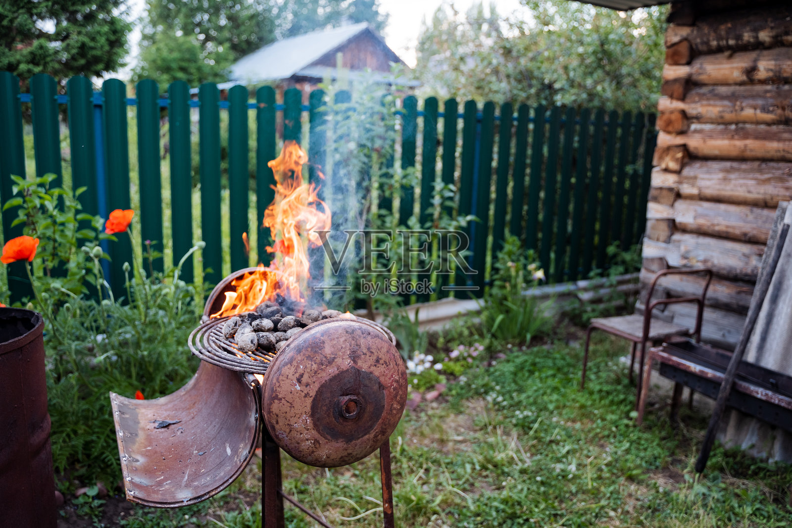 后院被明亮的燃烧桶照亮,周围环绕着植物、围栏、花盆和草坪,营造出自然与家居装饰相融合的温馨氛围。照片摄影图片