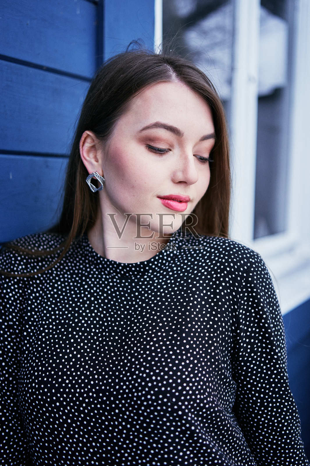 冬季时,一位长着金色长发的年轻女性穿着轻盈的裙子,站在蓝色谷仓旁的肖像。照片摄影图片