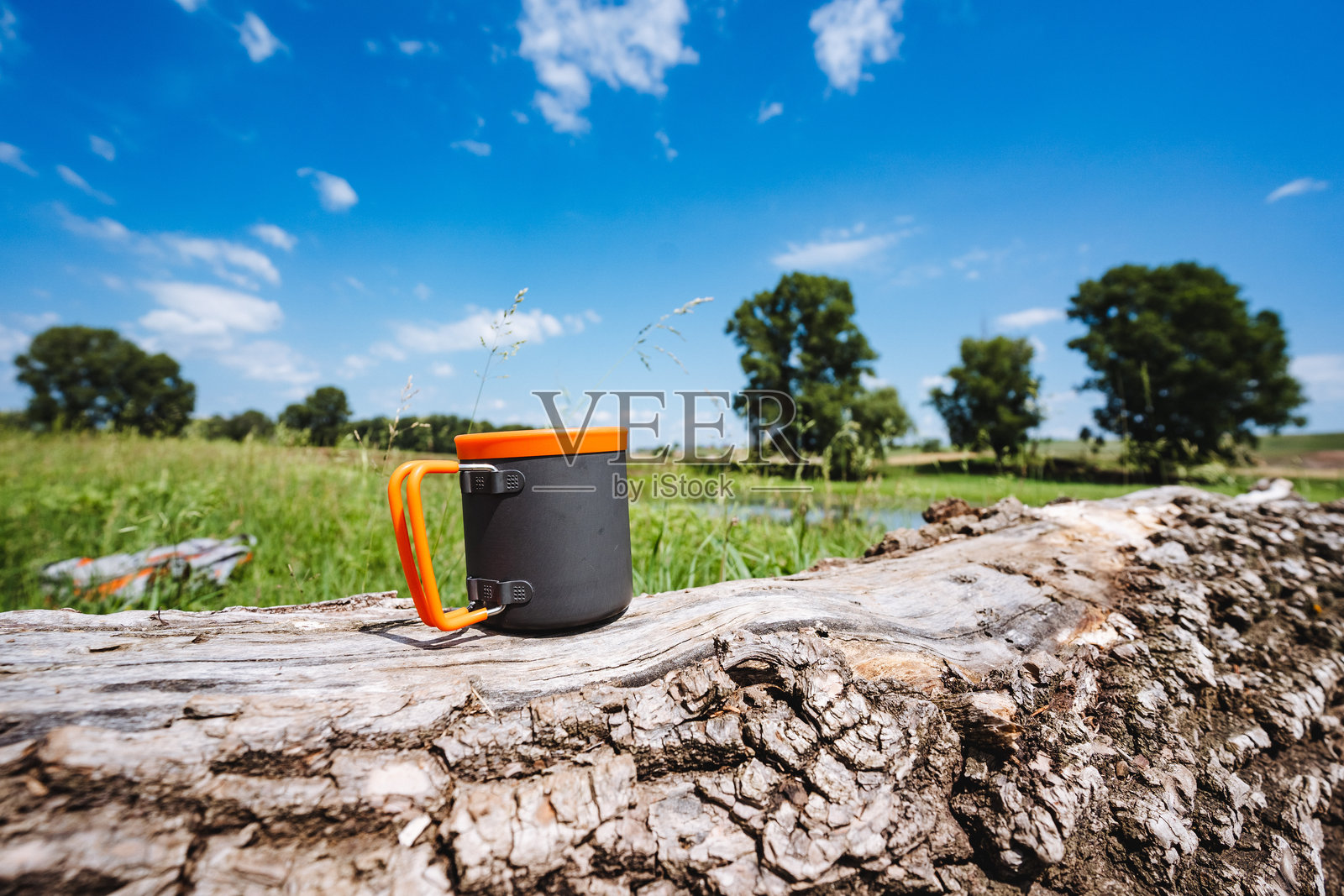 露营铝制杯子放在树桩上,背景是天空,茶具,金属杯,折叠手柄,硅胶唇边。照片摄影图片