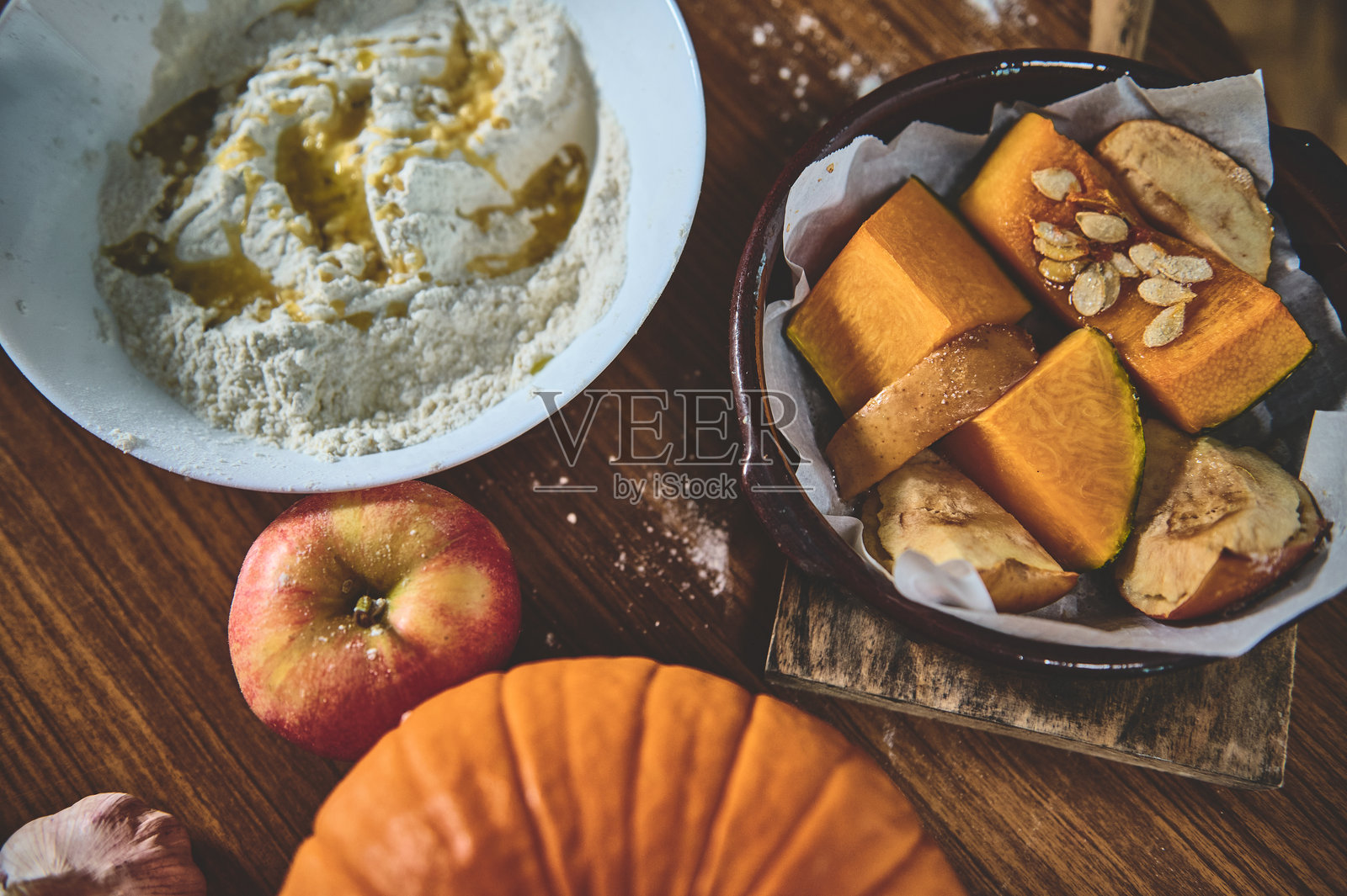 舒适厨房中带有南瓜、苹果和食材的乡村秋季烘焙准备,展示用于自制季节性馅饼或甜点的生面团和种子。照片摄影图片