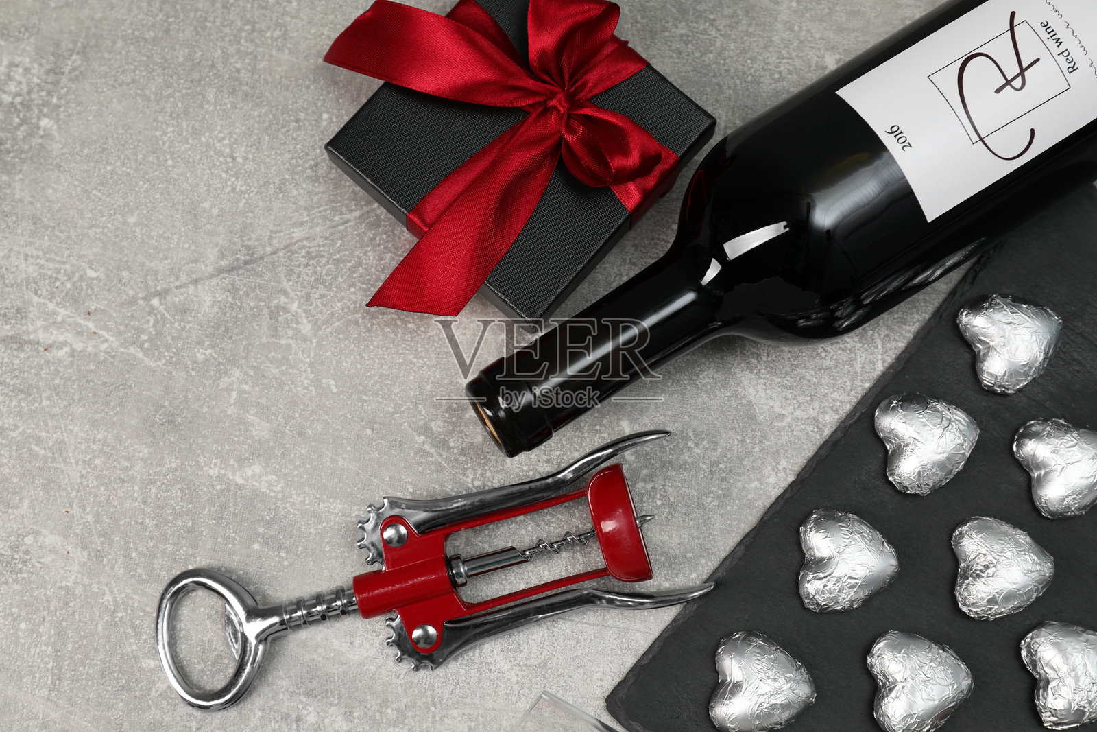 红酒瓶、心形巧克力糖果、开瓶器和礼品盒放在浅灰色纹理桌面上,俯视图照片摄影图片