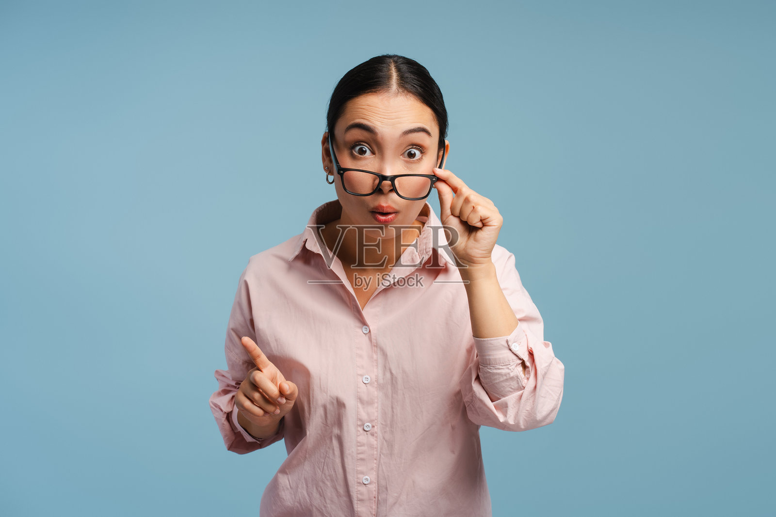 年轻的亚洲女性在蓝色背景下惊讶地指着前方。照片摄影图片