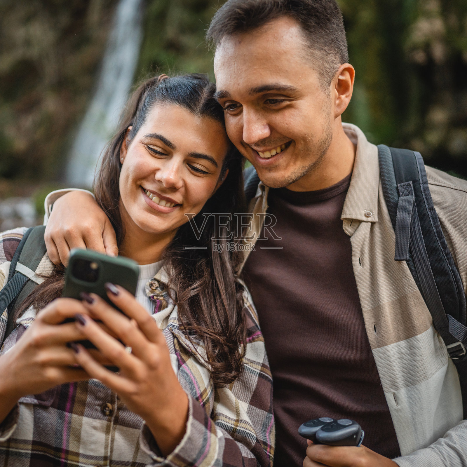 一对背包客情侣站在瀑布前使用手机照片摄影图片
