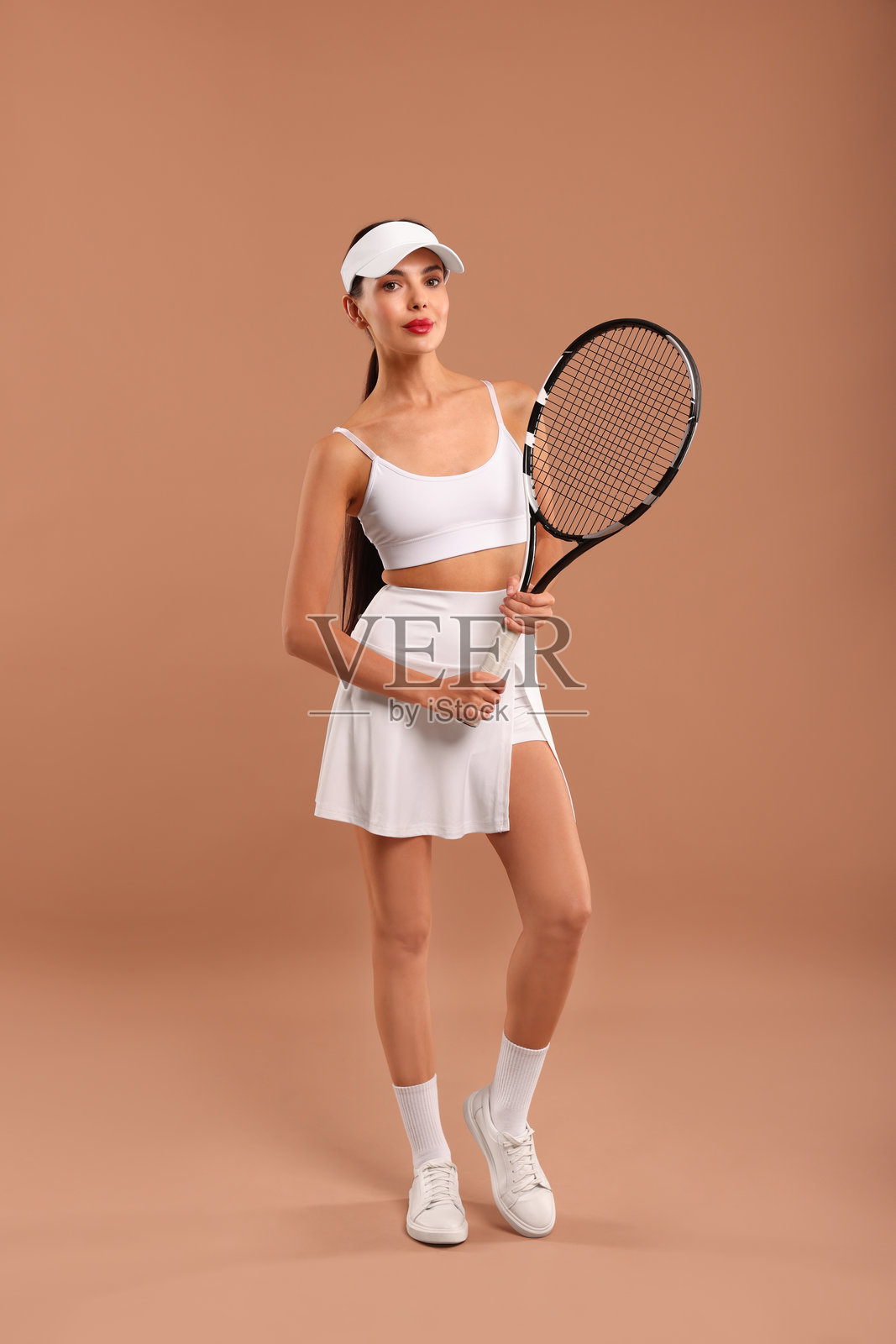 美丽的年轻女性手持网球拍,背景为棕色。照片摄影图片