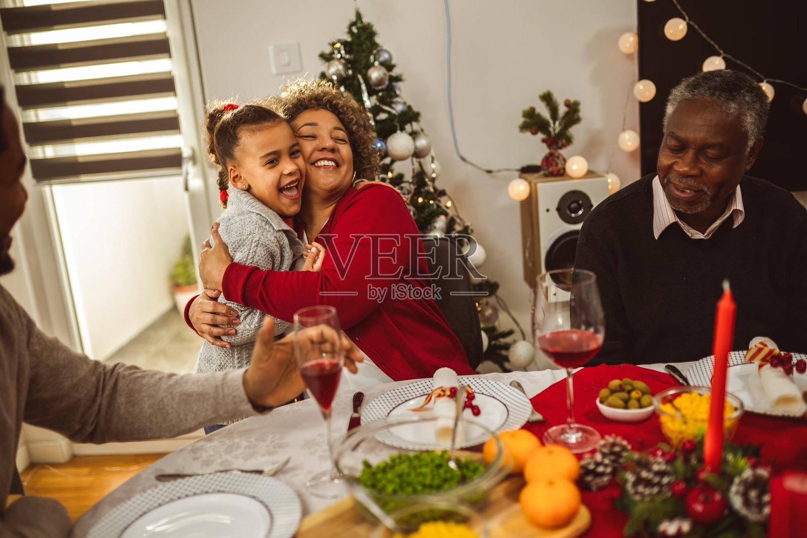非裔美国人孙女在感恩节晚餐时与祖父母拥抱。照片摄影图片