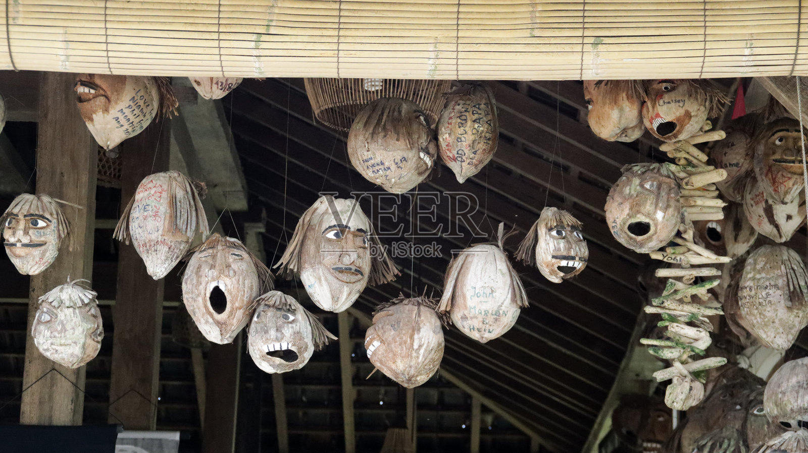 可怕的手工雕刻椰子脸挂在传统木屋内部,透入自然光。照片摄影图片