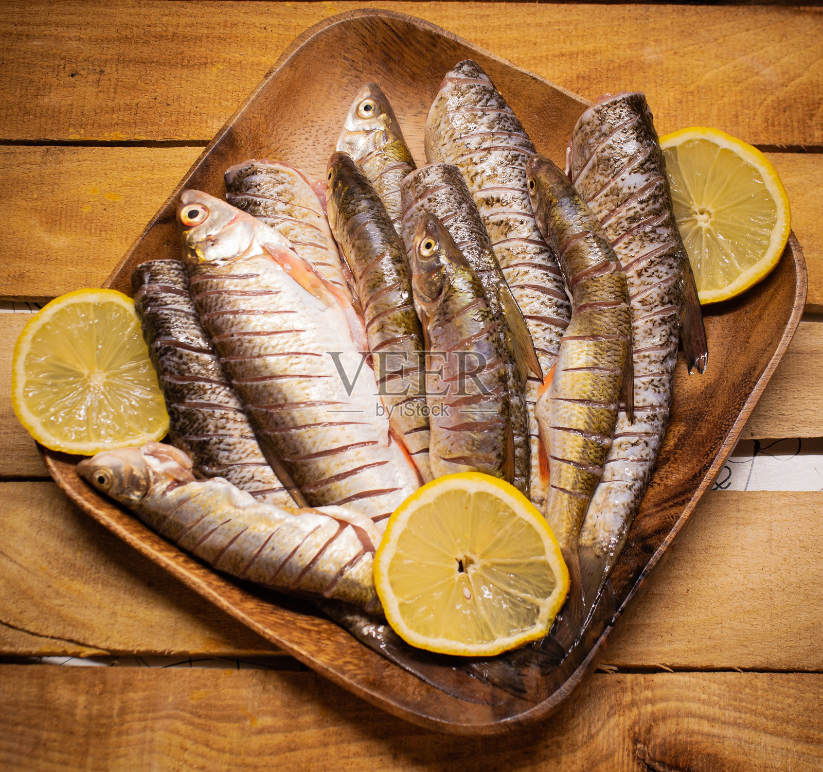 平铺的新鲜鲶鱼放在木质方盘上,背景是装饰有柠檬片的木质桌面。照片摄影图片
