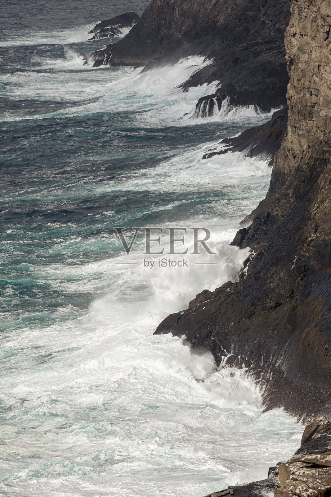 高耸的岩石悬崖沿海而立。岩石下的海面波涛汹涌,浪花拍打在岩石上,形成泡沫。照片摄影图片