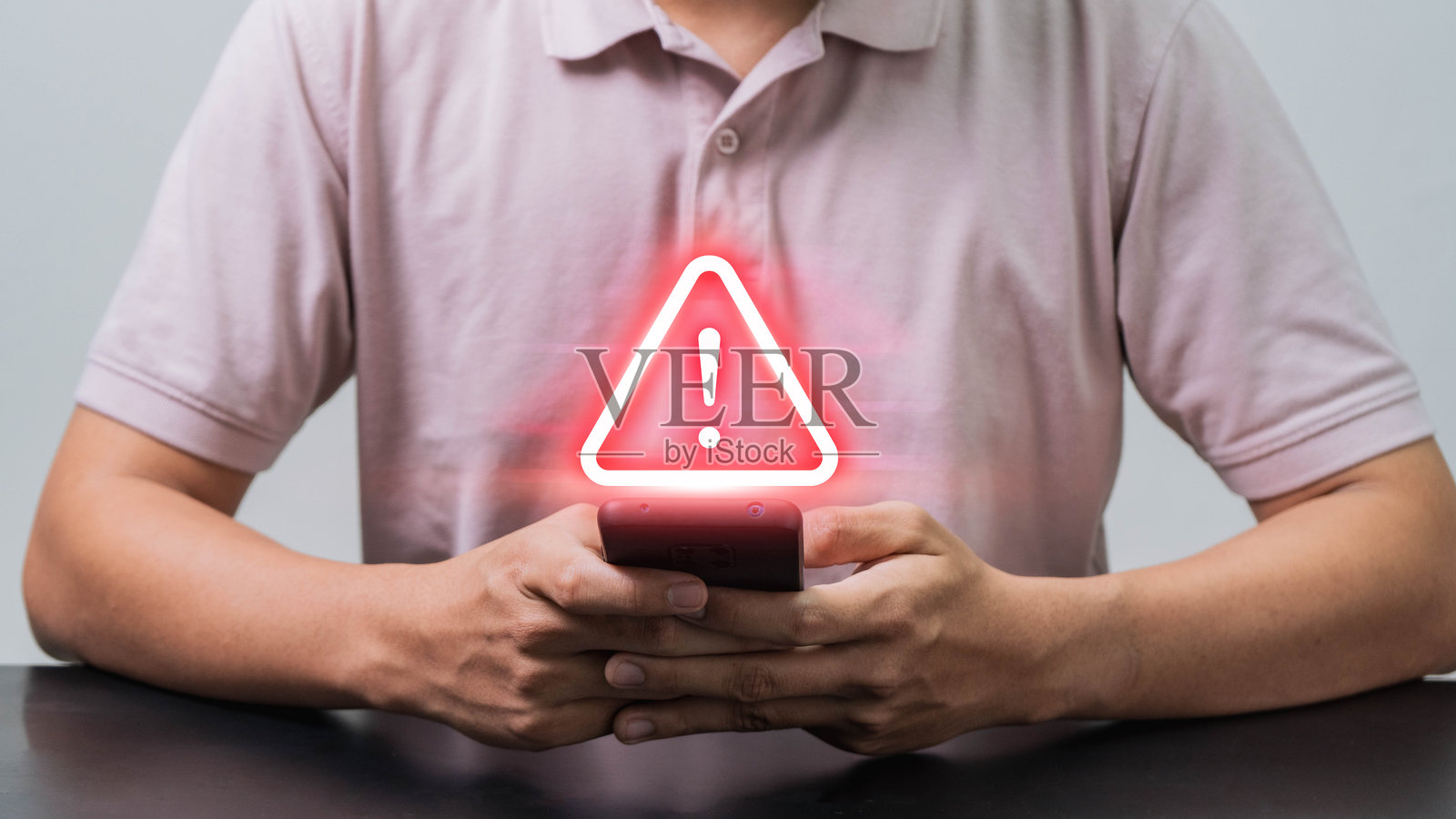 移动安全警报,一名男子使用智能手机,屏幕上显示诈骗警告符号,突显数字时代移动欺诈和网络诈骗日益严重的威胁。照片摄影图片