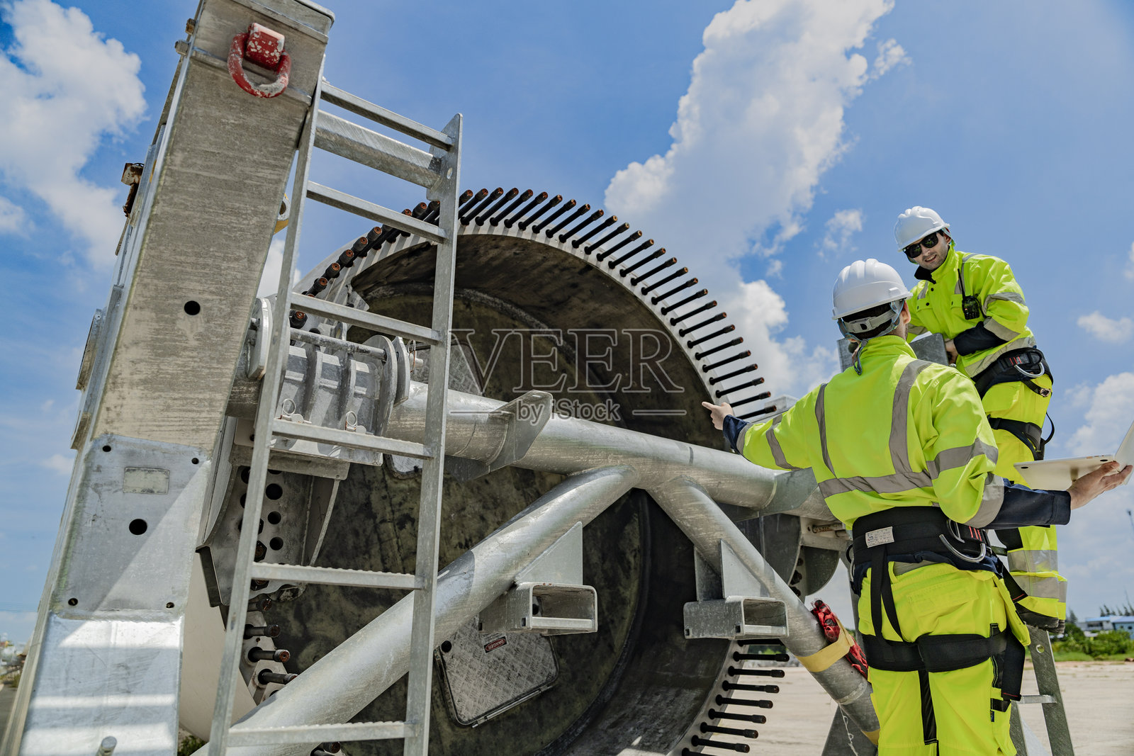 两名工程师在风力涡轮机组件上工作,一人使用笔记本电脑,另一人在梯子上检查零件。可再生能源技术、风能项目以及能源行业的团队合作。照片摄影图片