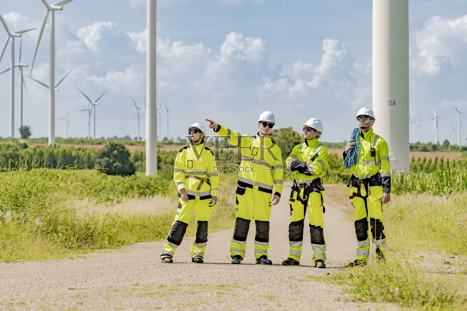 一群穿着高可视性装备的工程师走过风电场,背景中有风力涡轮机,强调团队合作、可再生能源和风能技术。照片摄影图片