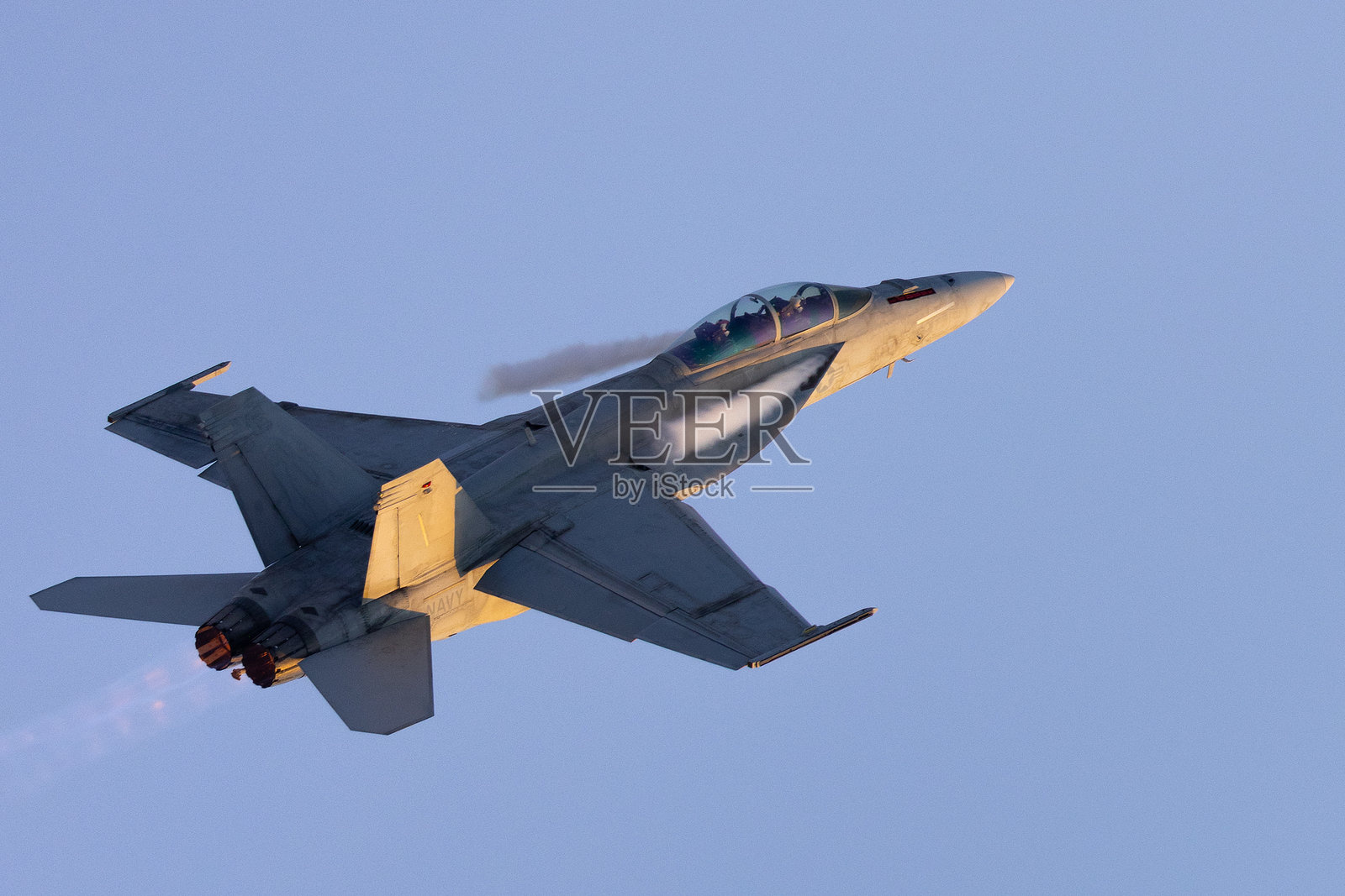 F/A-18F超级大黄蜂战斗机尾部视角,沐浴在日落的余晖中,机翼根部有凝结尾流,后燃器开启。照片摄影图片