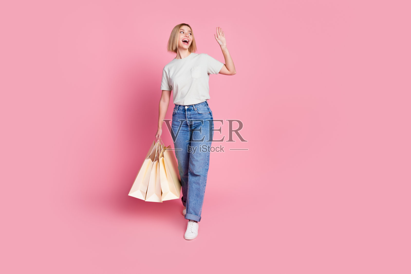 可爱的快乐女孩穿着时尚的灰色衣服,手提包裹,望向空旷的空间,背景为粉色。照片摄影图片