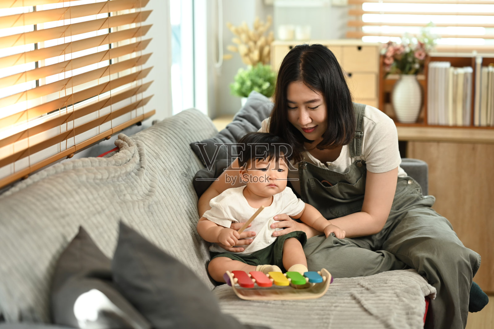 美丽的年轻母亲和小男孩在家里的沙发上玩玩具。育儿、儿童照护和家庭概念。照片摄影图片