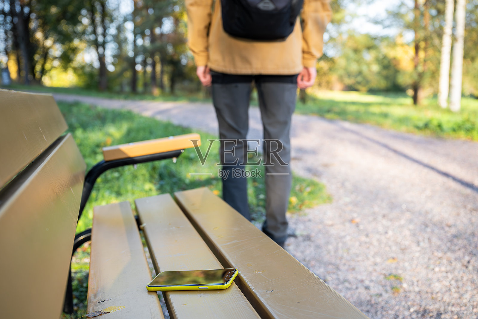 男人离开长椅,遗落智能手机在公园长椅上照片摄影图片
