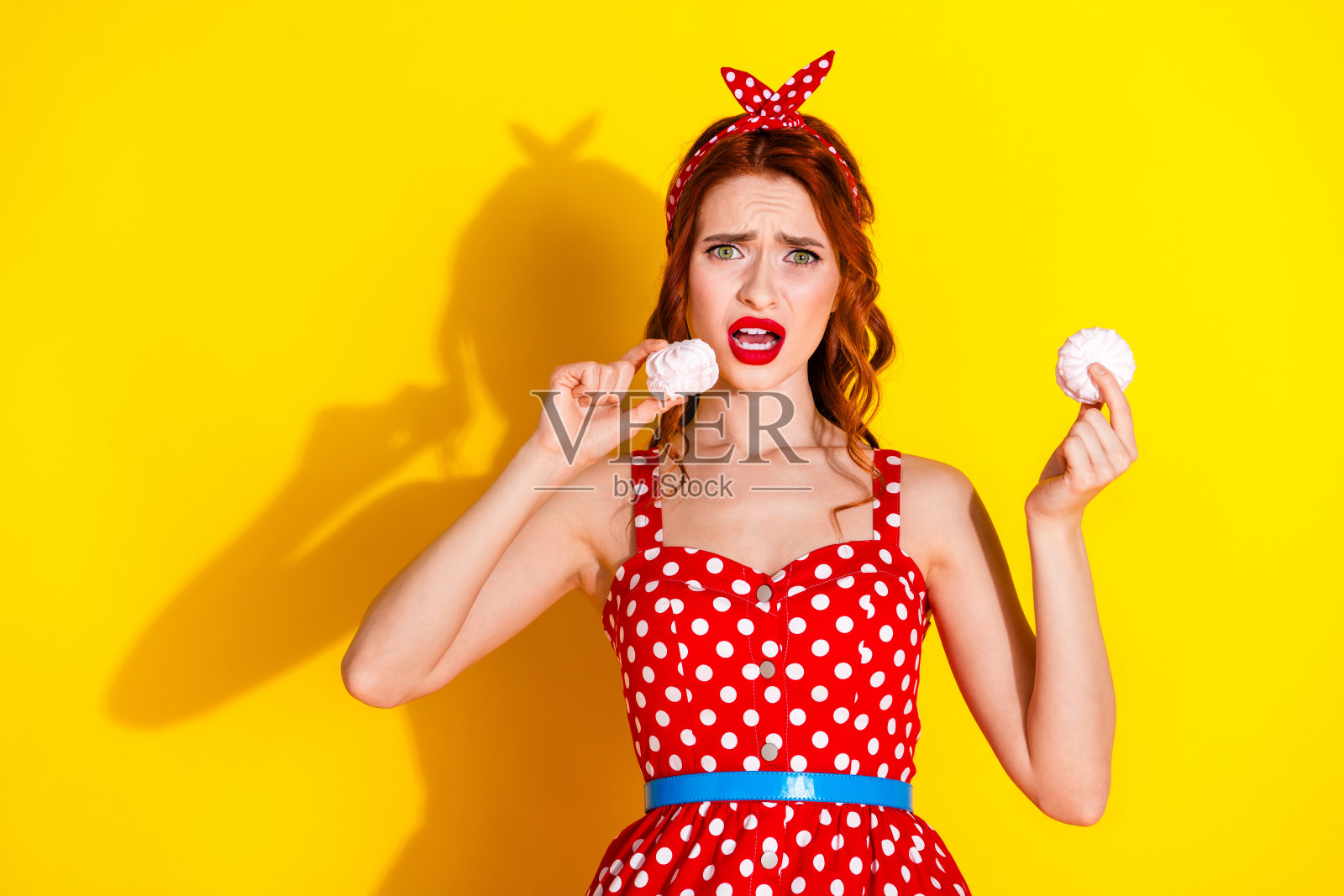 可爱的漂亮女士穿着红色时尚服装,手中拿着美味的棉花糖,背景为黄色。照片摄影图片