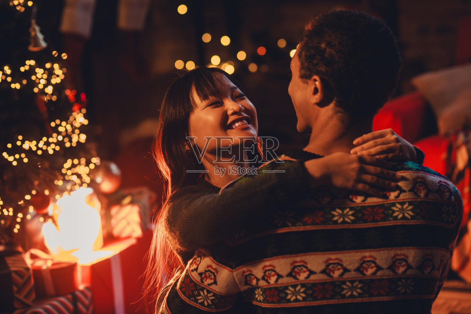 年轻情侣穿着圣诞服装,享受温馨的圣诞派对,互相拥抱,玩得开心,室内装饰温馨。照片摄影图片