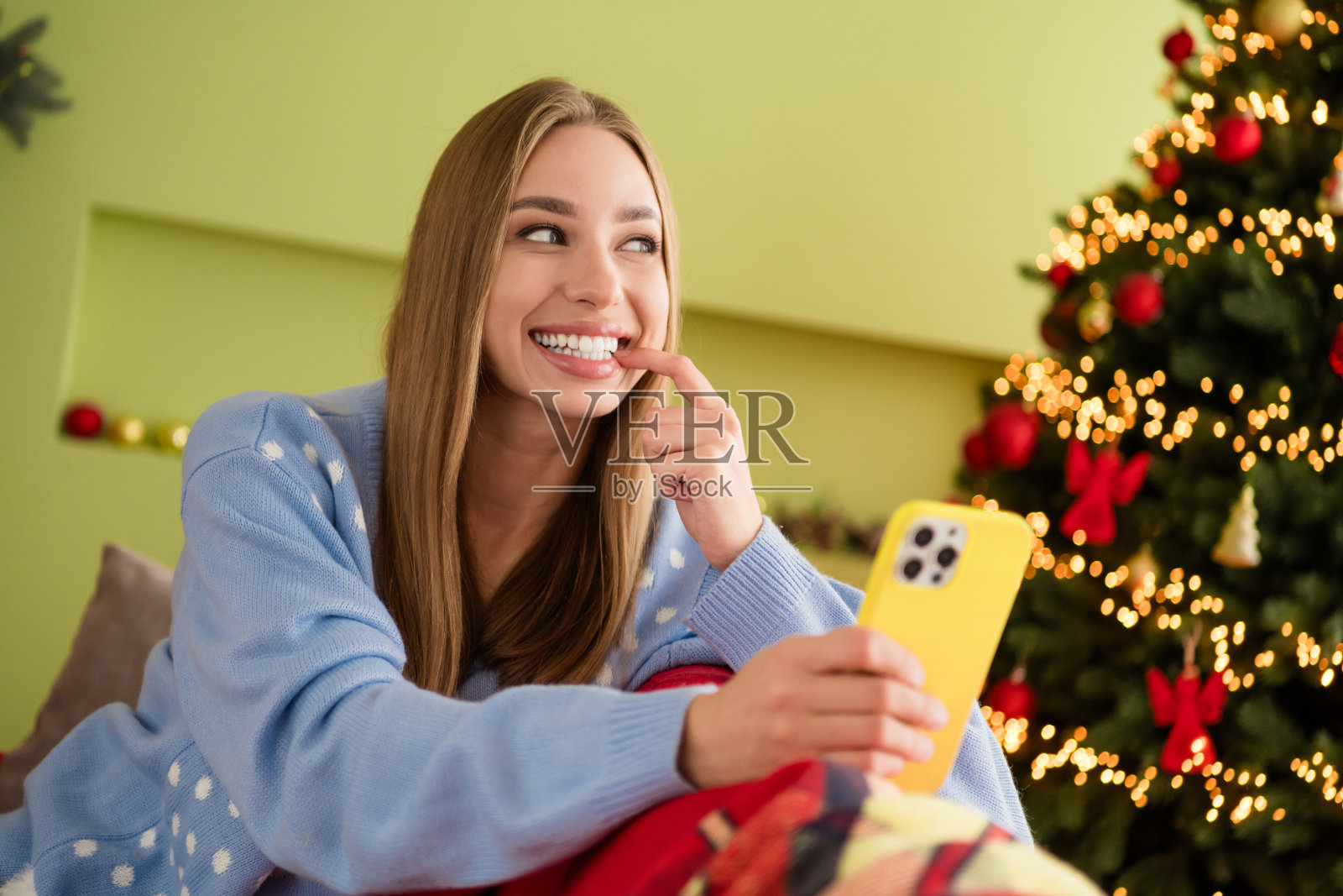 年轻迷人的金发女友躺在沙发上用智能手机选择圣诞礼物。照片摄影图片